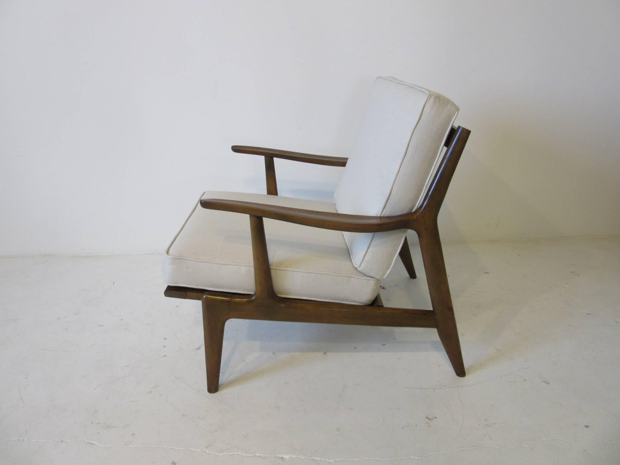 A wood frame Italian lounge chair with two loose box upholstered cushions in the manner of a Danish chair from the period. Upholstered in a beige linen and having sculptural wood back braces and front leg detail, retains the label Made In Italy.