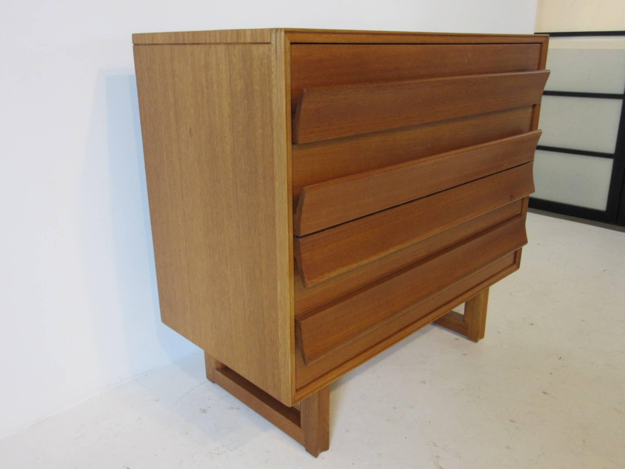 A four-drawer chest with winged pulls and architectural styled base in ribboned Indonesian mahogany, retains the manufactures label to the inside drawer, Paul Laszlo for the Brown Saltman furniture company.