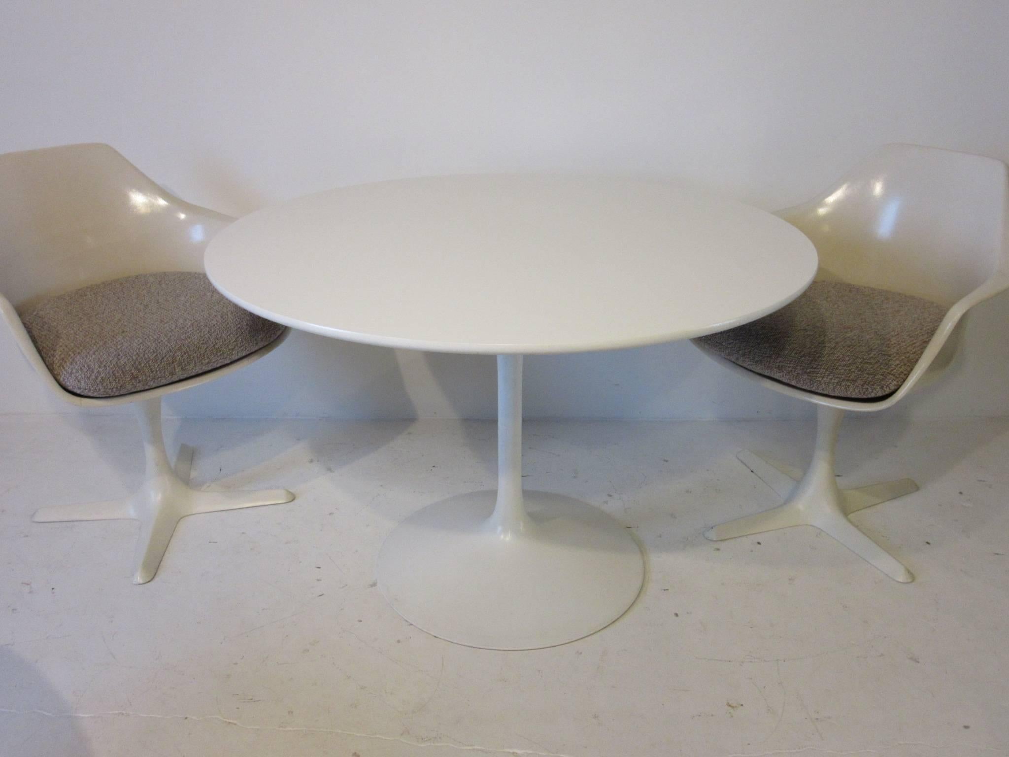 A white tulip dining table with matching laminate top and four X based swivelling armchairs all with sand, cream ,taupe salt and pepper upholstered contract fabric cushions . Manufactured by the Burke Furniture Company. The table diameter