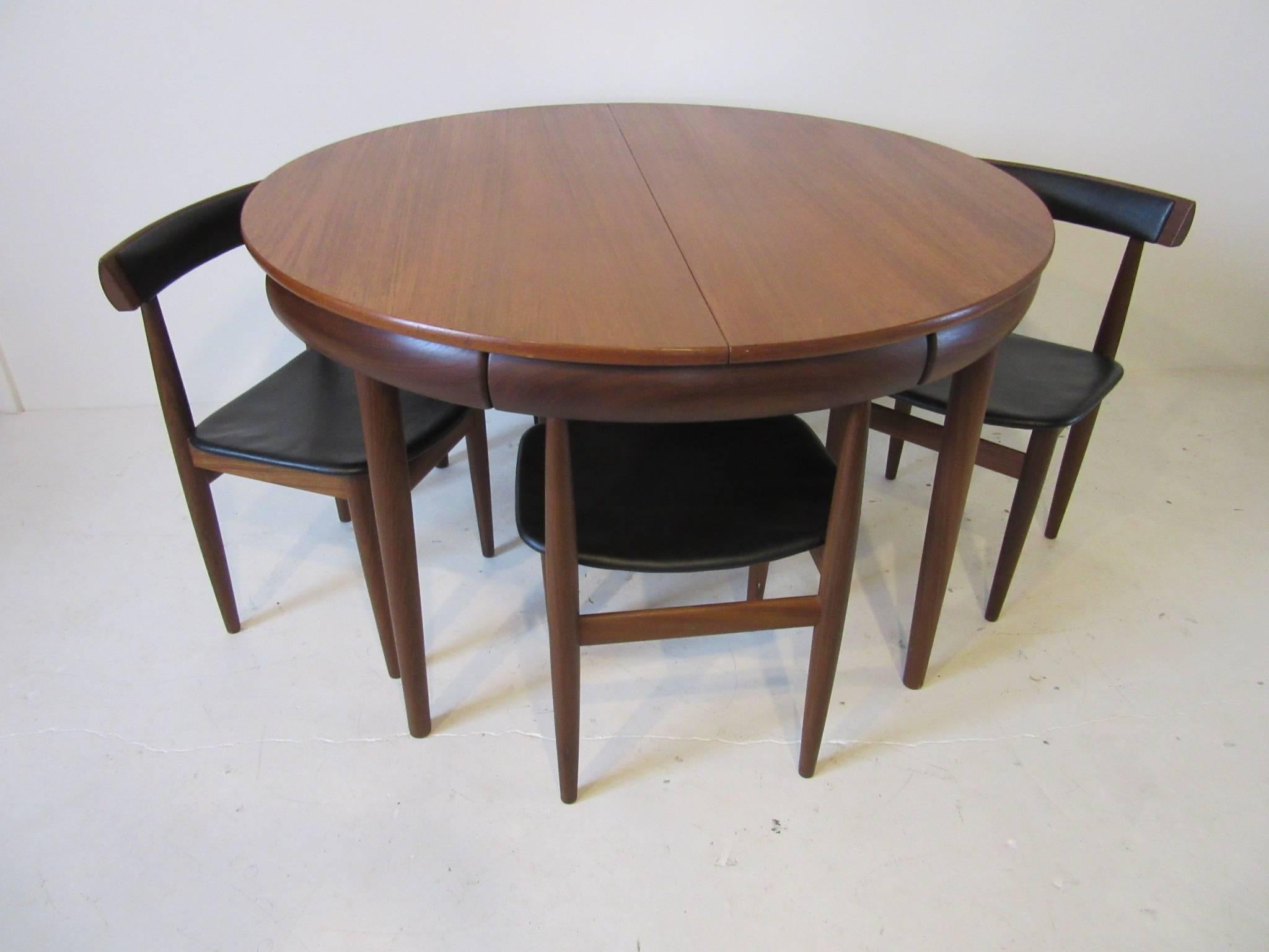 An expanding dining table with flip up hidden leaf and four chairs that integrate into the top of the table to form a perfect circle. The top is constructed of light teak and the chairs and table frame from very dark teak wood. An interesting space