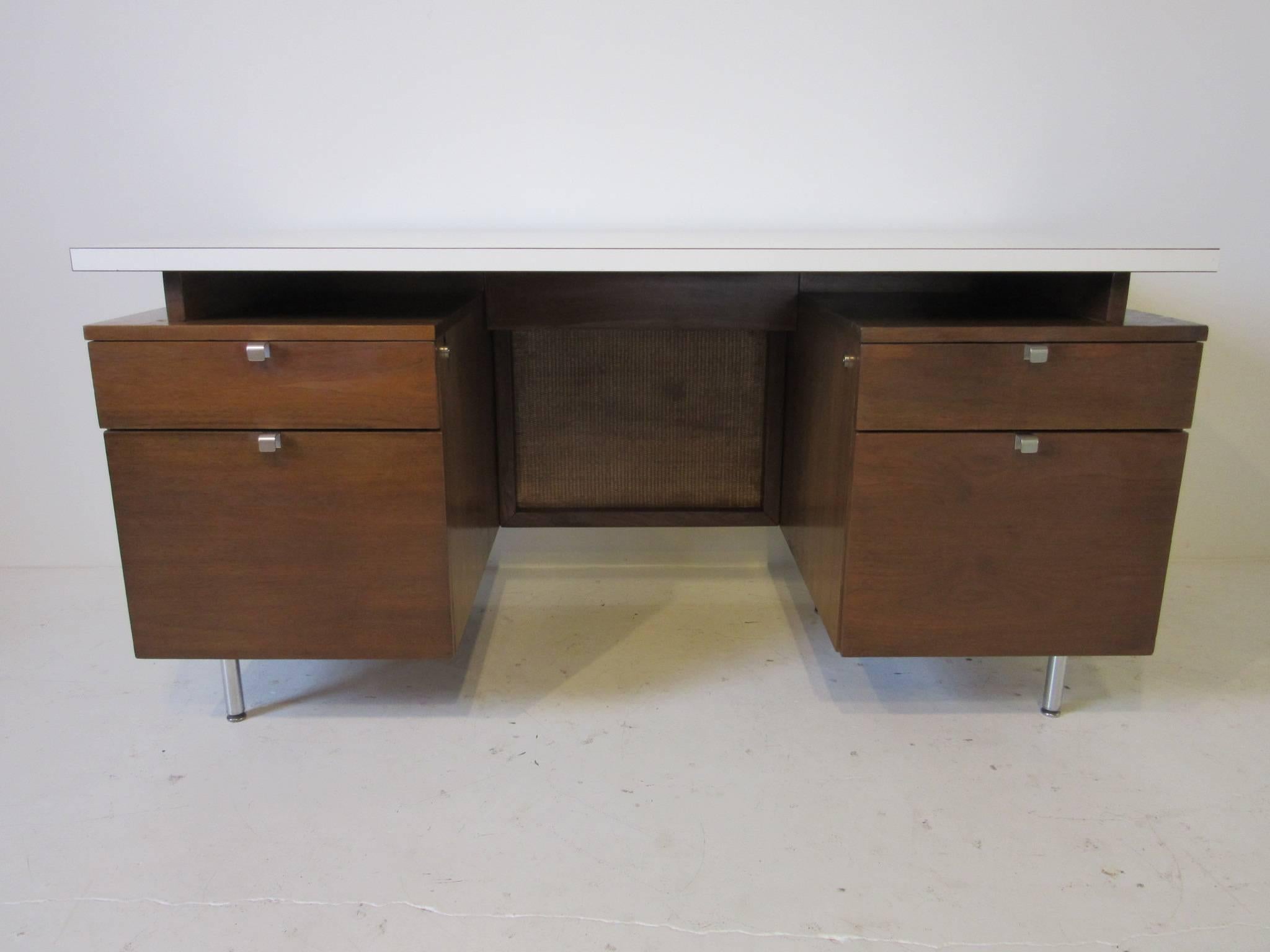 A walnut four-drawer desk with aluminium J pulls, chromed steel legs, woven privacy panel and topped in white Laminate fitted for a bank building. The National Historic Landmark was designed by Eero Saarinen and was completed in 1954 using furniture