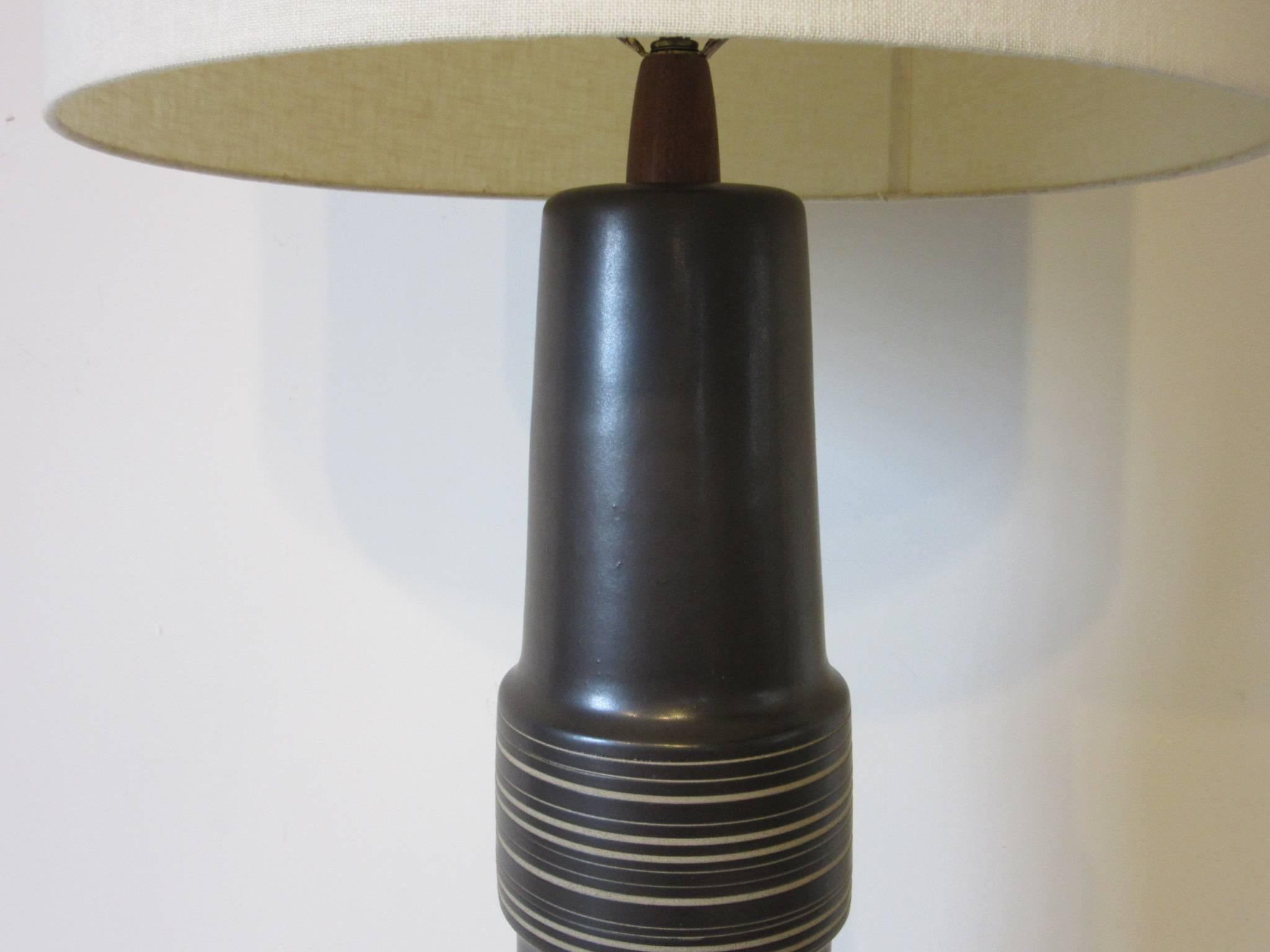 A large sized Martz table lamp in a dark chocolate and charcoal toned glaze with incised body designs in a sand color. The lamp stem and finial are made of teak wood and the piece is artist signed to the lower backside, Martz, produced for Marshall