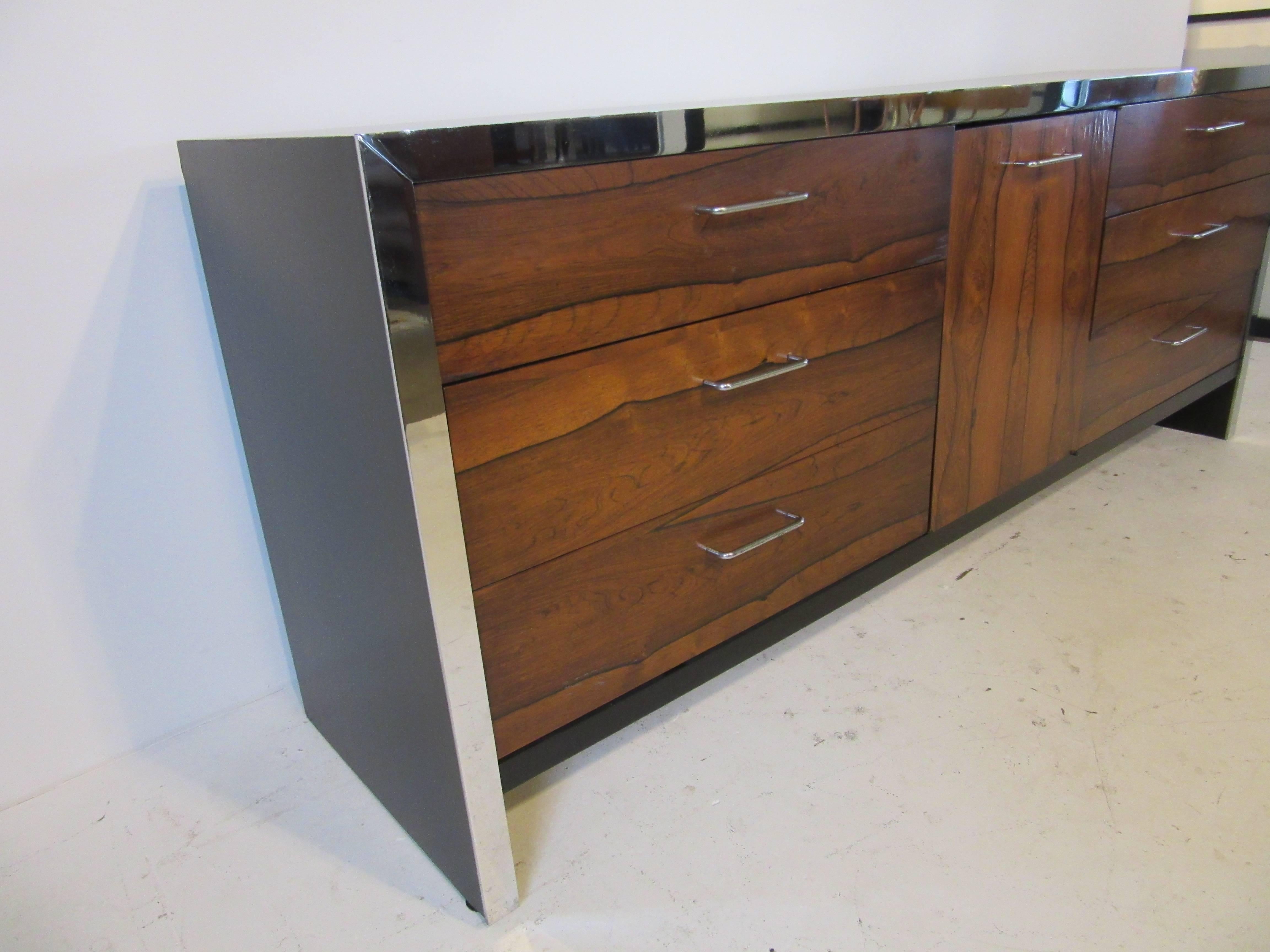 A nine-drawer dresser with three drawers behind a wonderfully grained rosewood door, chrome defining front trim with matching pulls and satin black wood cabinet. In the style of Milo Baughman.