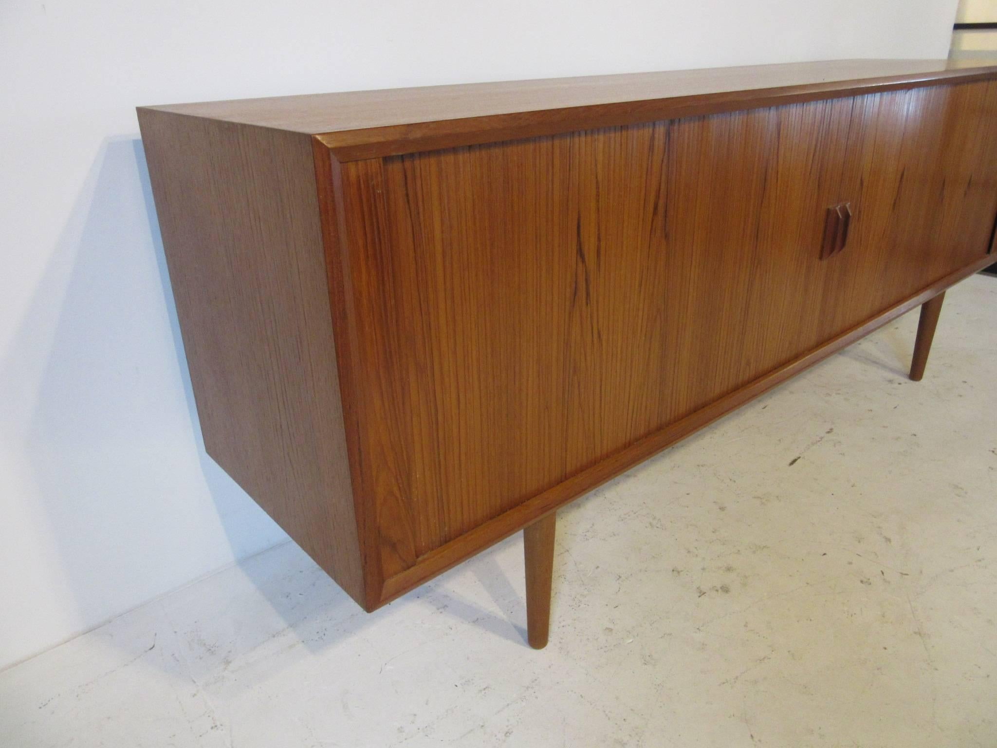 A well crafted teak wood credenza with two sliding tambour doors, four slim drawers with felt lining and three adjustable shelves and storage. Great gaining to the front and wood pulls all sitting on matching conical legs and a finished back side so