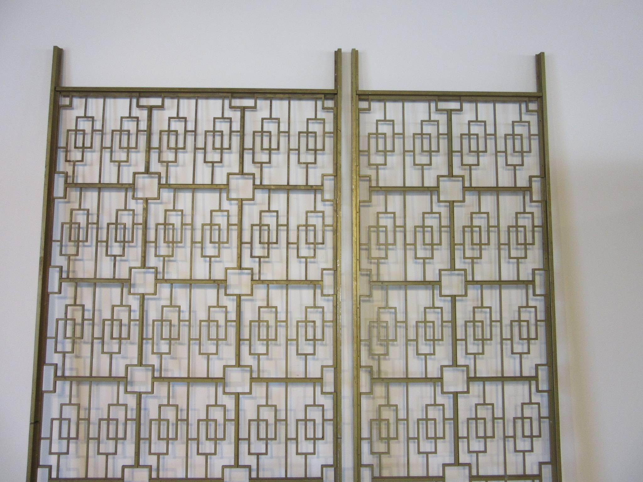 A two-piece cast aluminum architectural decorative room divider or screen painted in a brass tone with screwed together design sections mounted on flat bars for installation. Well crafted and excellent for that entrance way or room that needs some