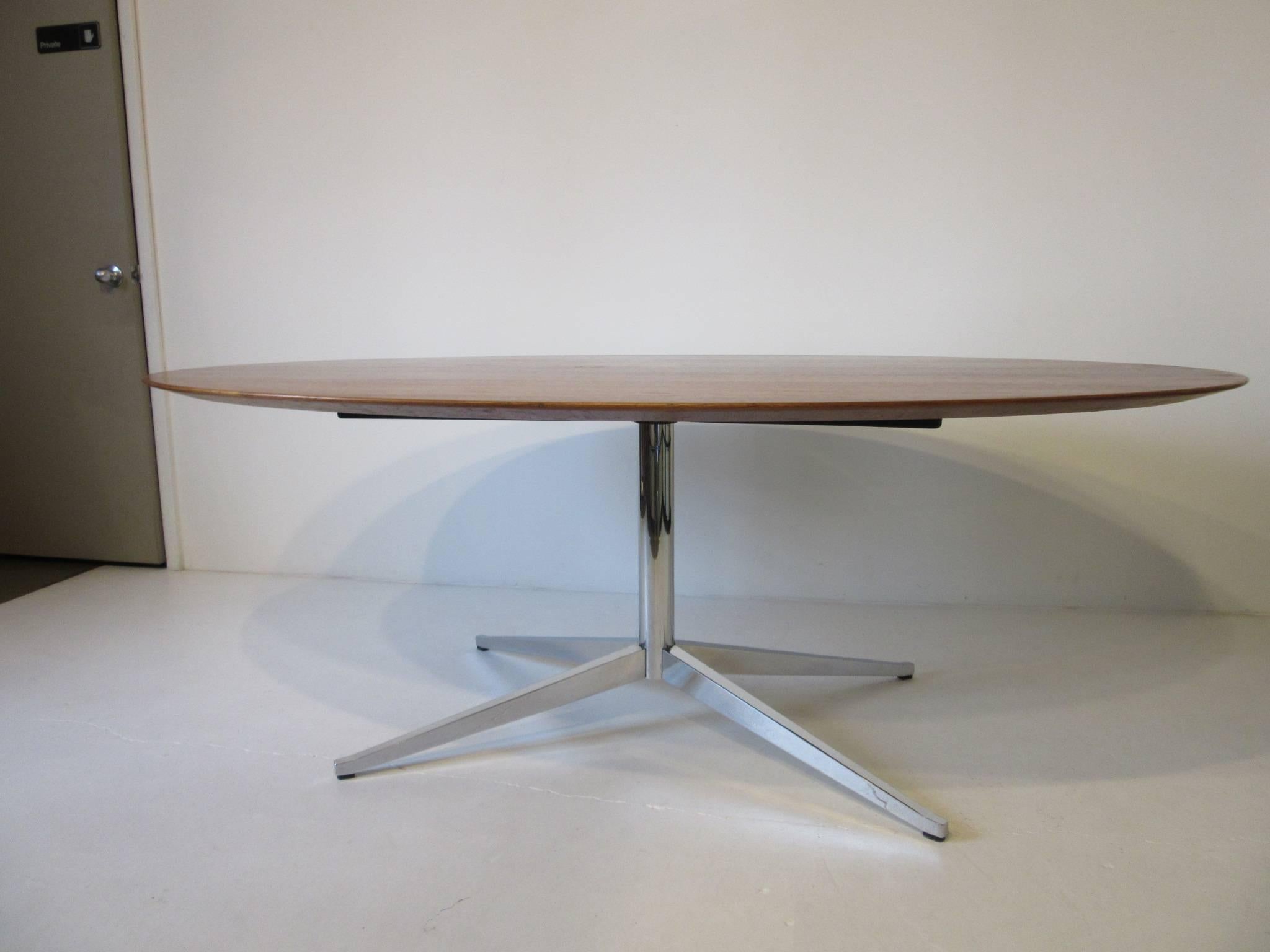 A well grained medium colored oval walnut dining or conference table in a satin finish with a heavy gauge welded steel X-base in polished chrome. Manufactured by Knoll International and designed by Florence Knoll.