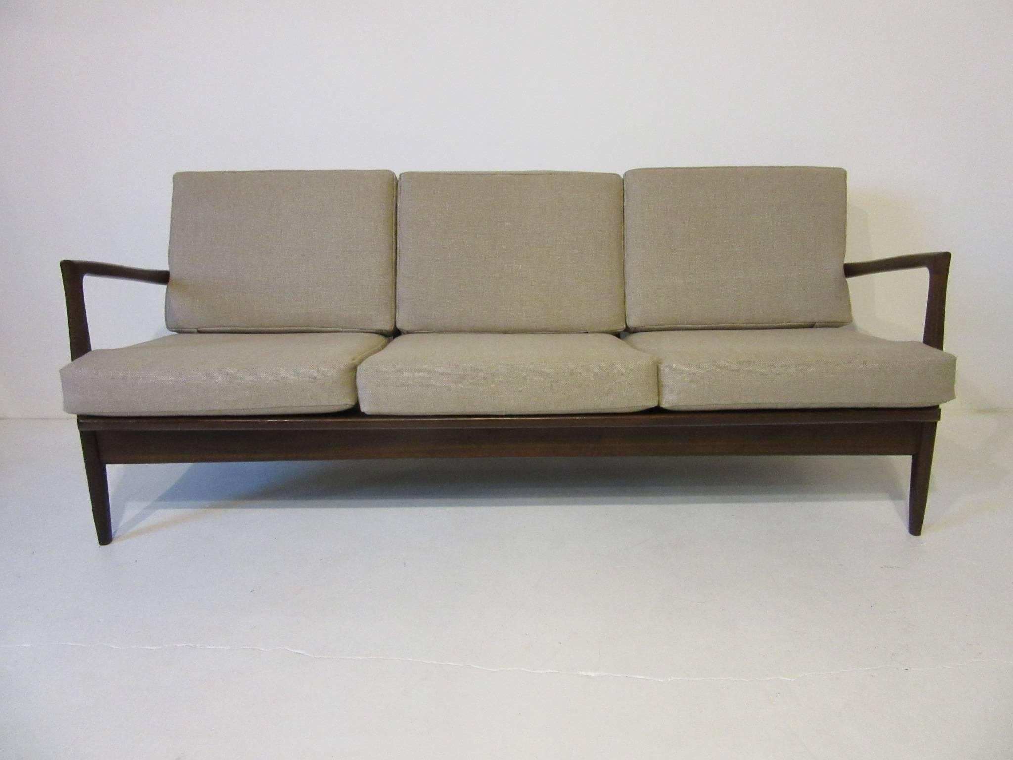 A Jensen sofa with dark sculptural wood frame and six loose cushions in a medium sand toned woven linen. The wood back rests have that trademark angled boomerang design so typical of Poul Jensen, manufactured in Denmark for Selig.