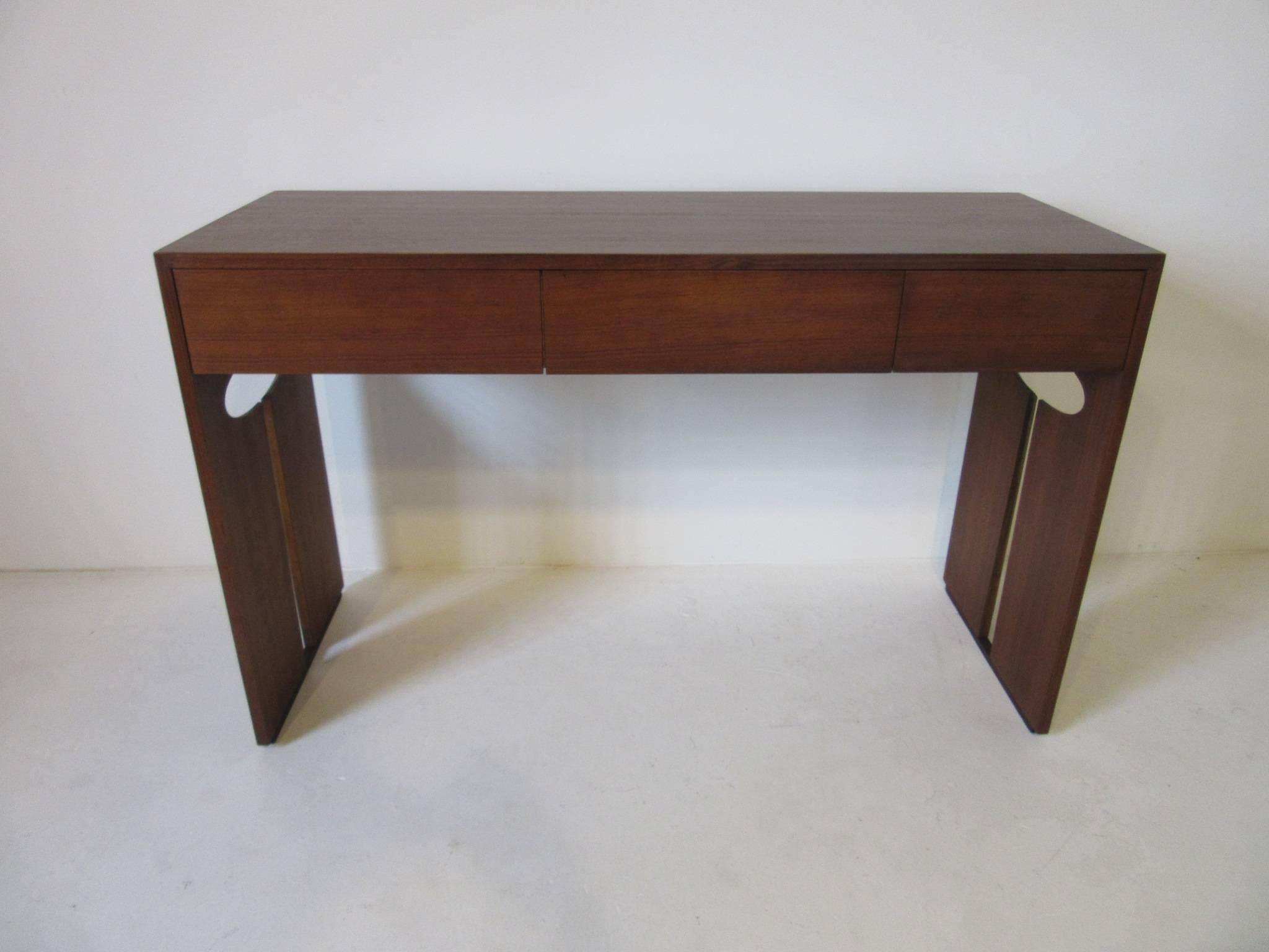 A smaller sized dark walnut desk with three drawers and legs with key hole cut-out design, perfect for a tight space with a modern look and designed in the style of Henry P. Glass.