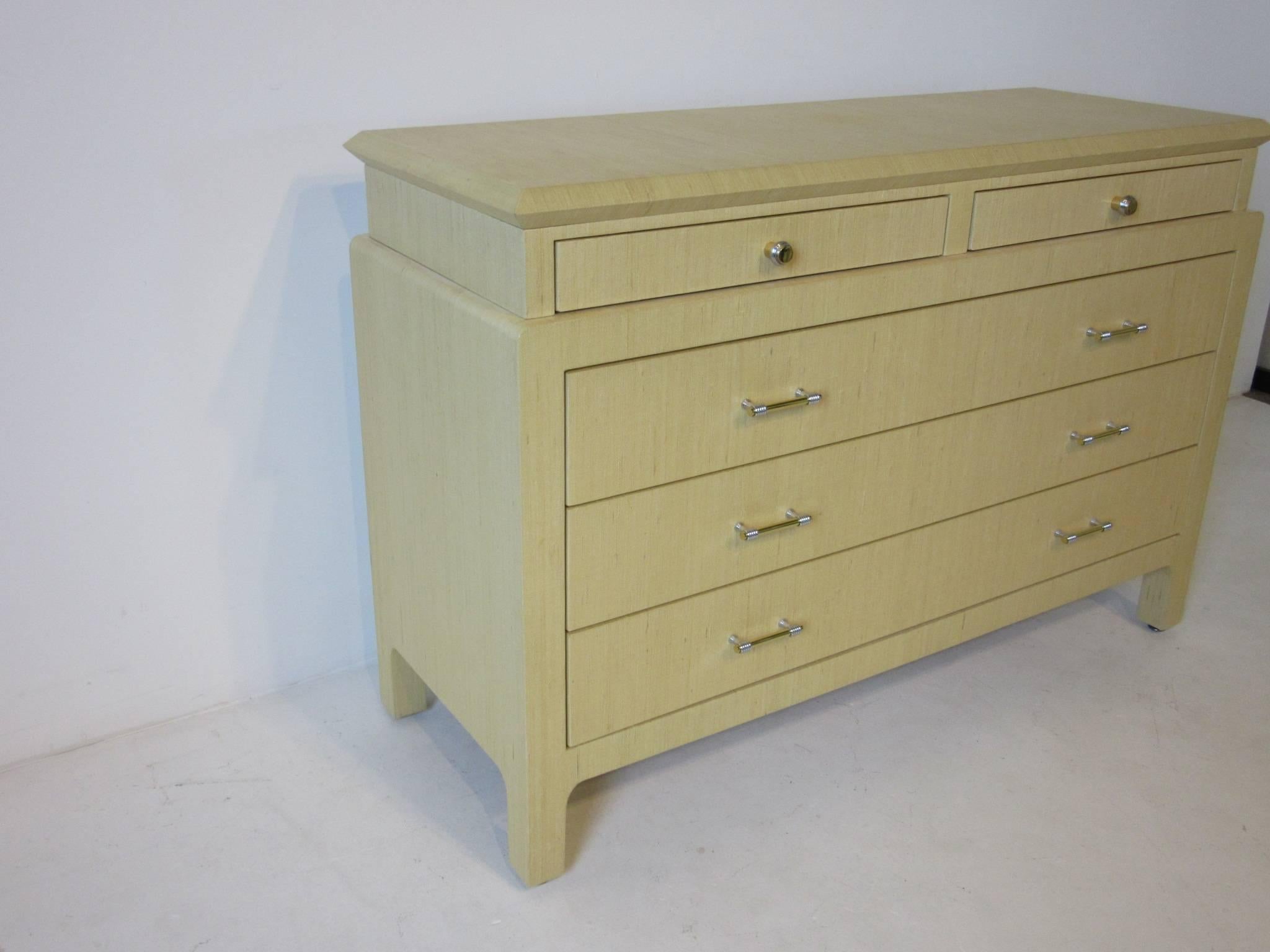 A well crafted dresser commode linen wrapped and lacquered in a nice mellow sand tone with two small upper drawers and three large lower drawers. Chromed wrapped brass hardware finishes off the chest designed in the manner of Karl Springer  .