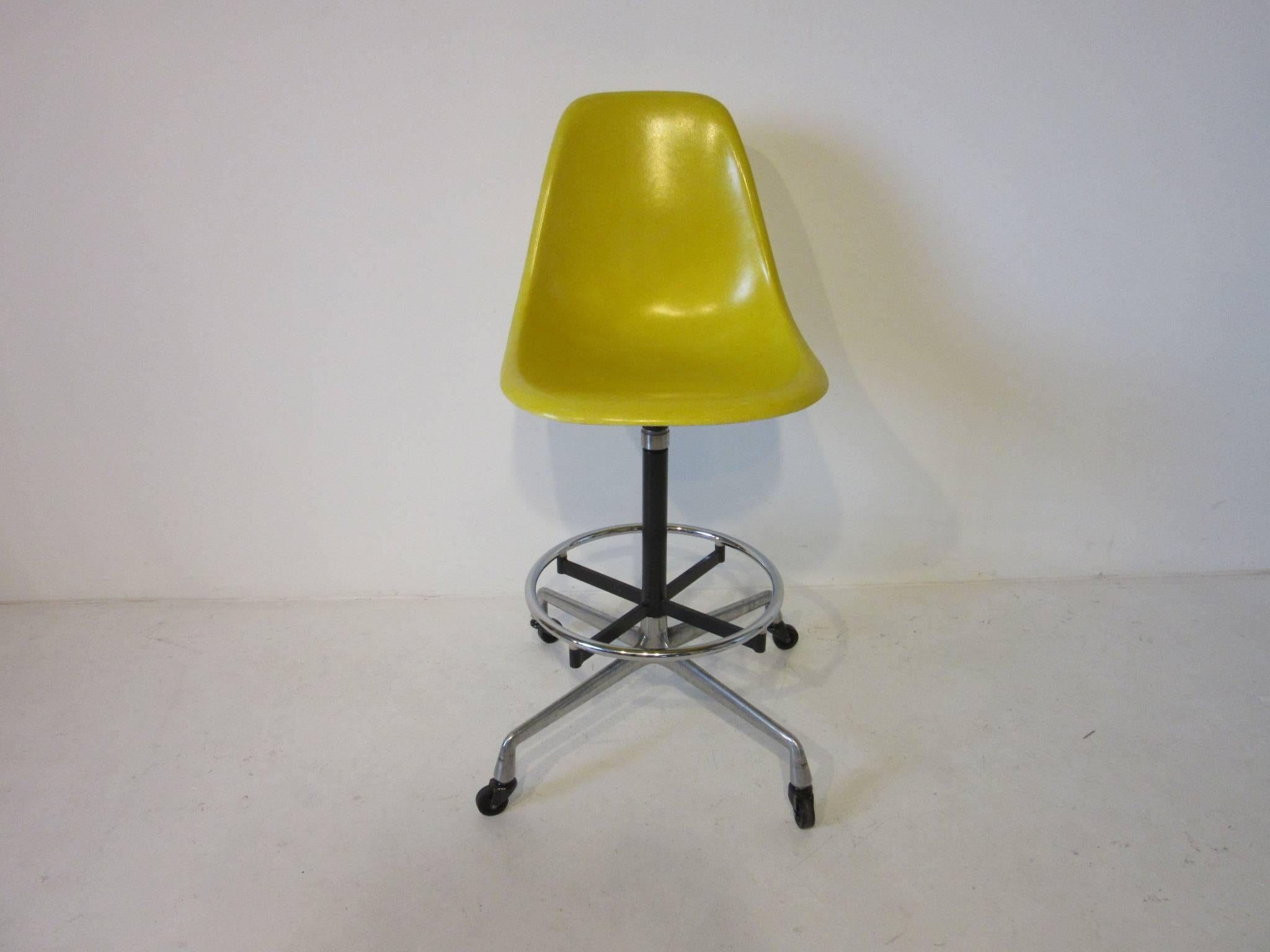 A pair of Eames aluminium group swiveling and height adjustable rolling architectural drafting or bar stools with bright yellow fiberglass shell seats. Dark grey metal support frame with chromed footrest and cast aluminium base with black wheels