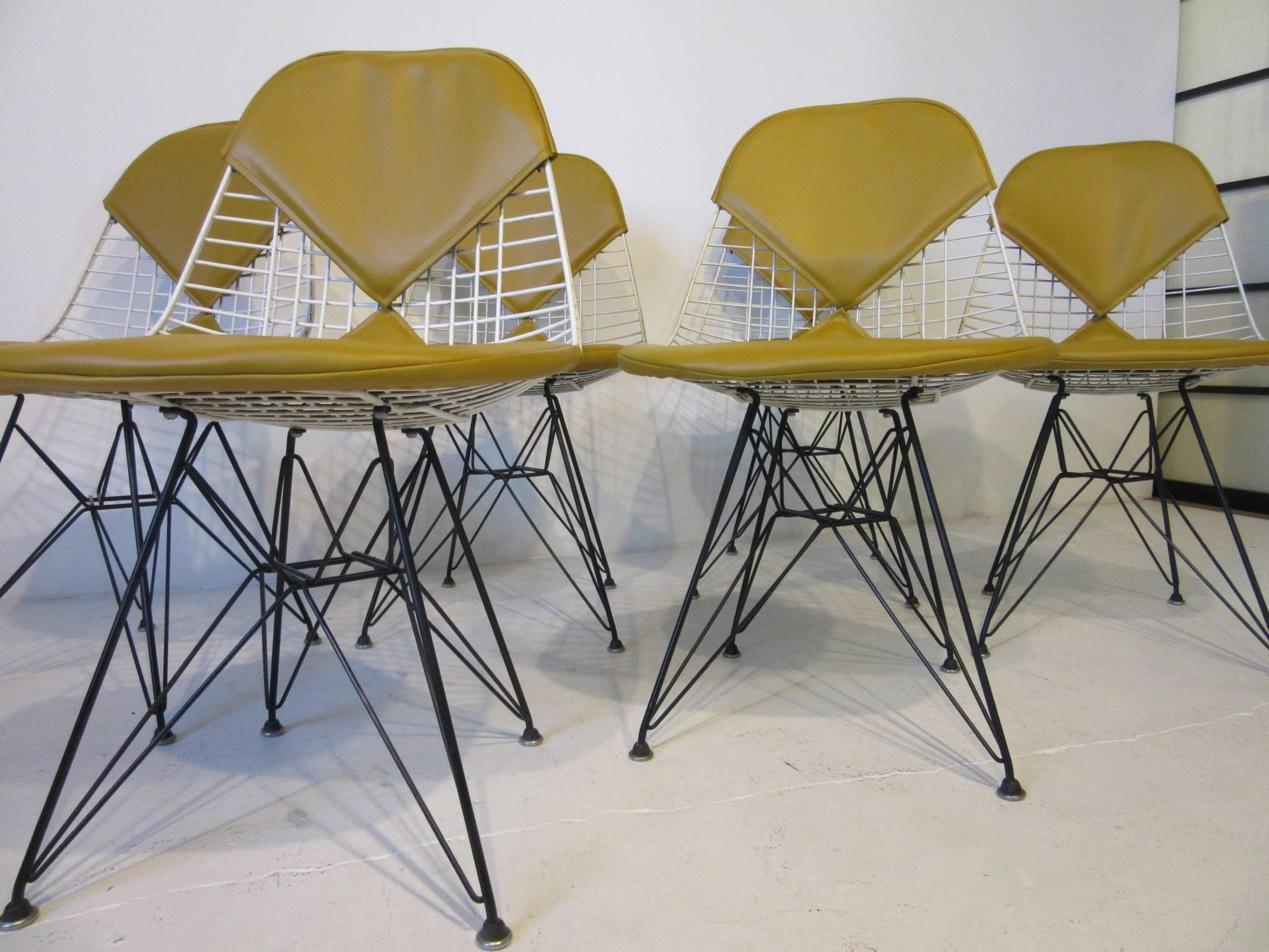 A set of six white wire seat Eiffel tower dining chairs with satin black bases, domes of silent feet and butter scotch Naugahyde bikini seat cushions . Made by the Herman Miller Furniture Company.