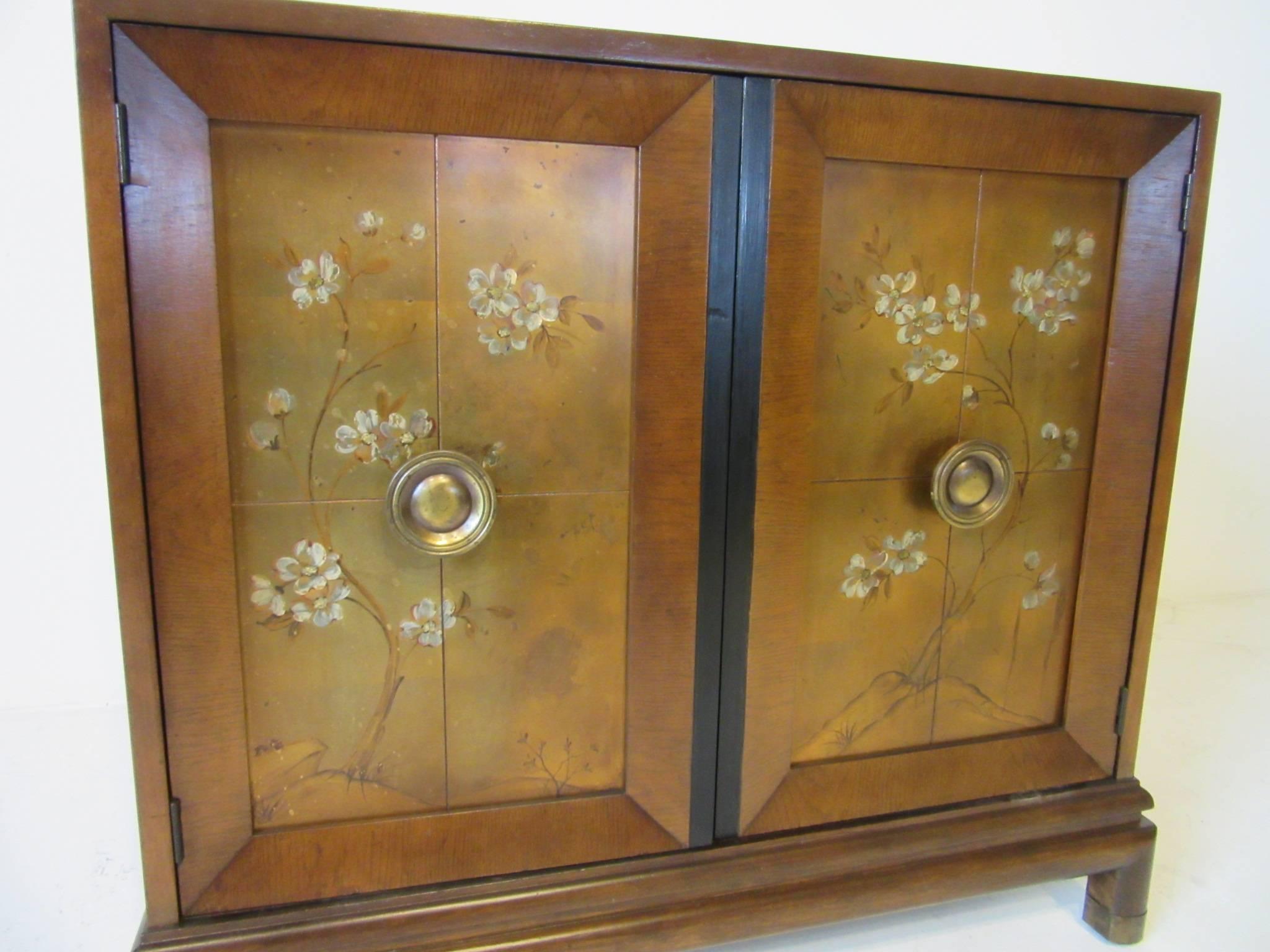 A decorated double door commode or cabinet with gold leaf and painted front, mahogany and black detailed chest with brass pulls and feet caps. Made by the Johnson Brothers Furniture Company.