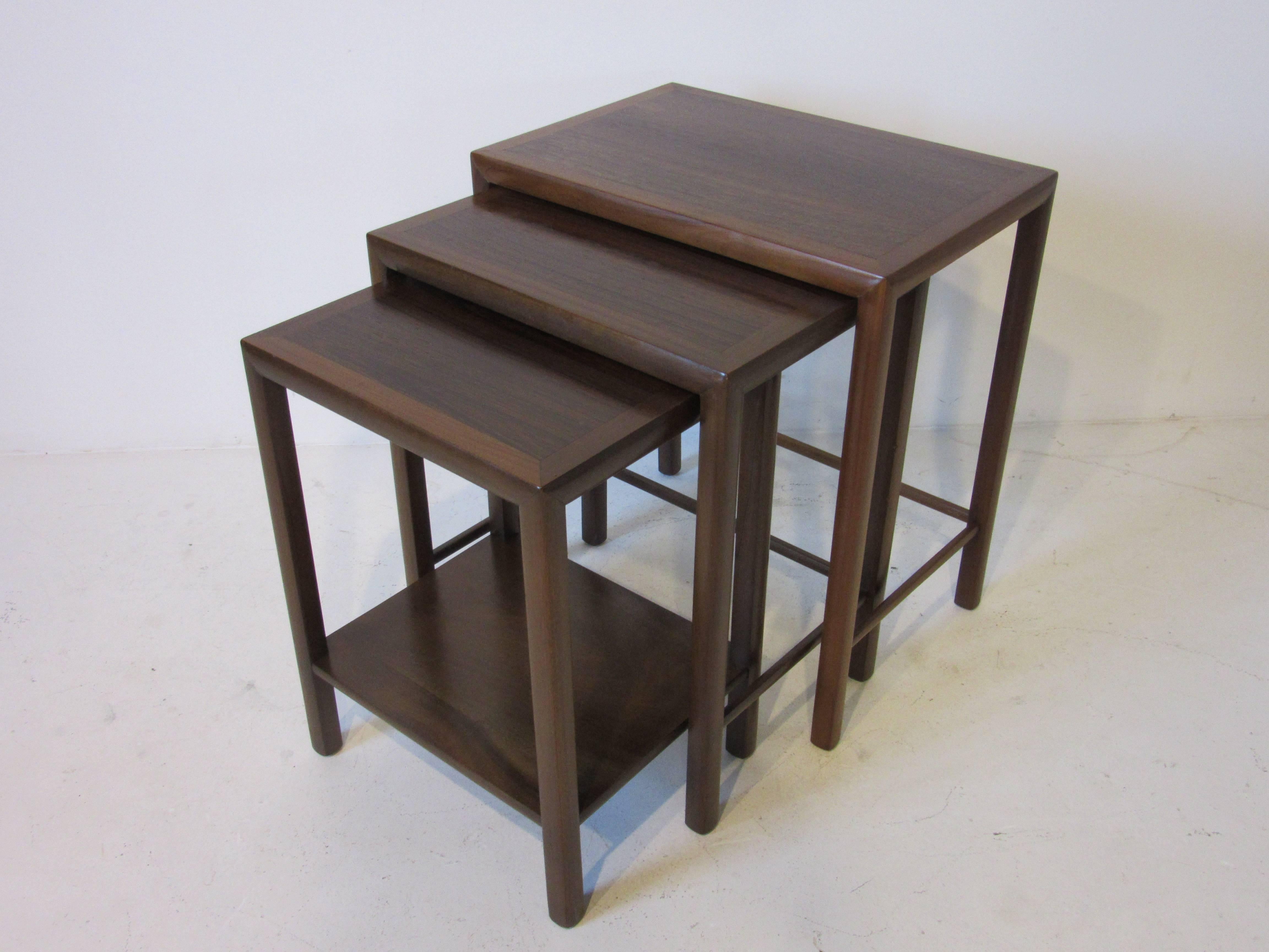 A set of three nesting tables with dark walnut frames and inserted rose wood table tops. The smallest table has a shelve to the bottom and the others have all matching wood stretchers all neatly fitting together. Manufacturers imprint to the bottom