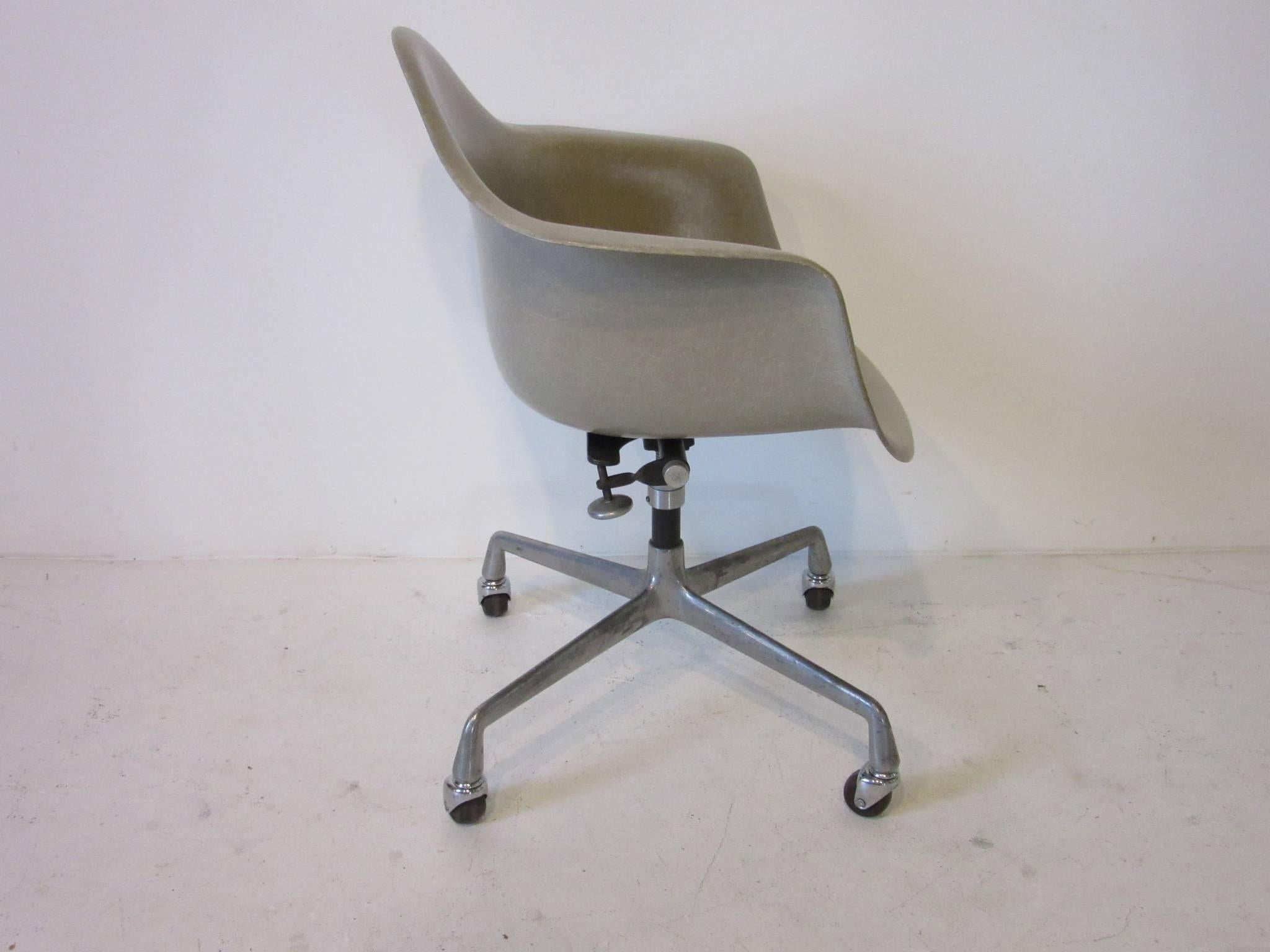 A taupe or greige toned fiberglass arm shell swivelling desk chair with cast aluminium rolling base manufactured by the Herman Miller Furniture Company.