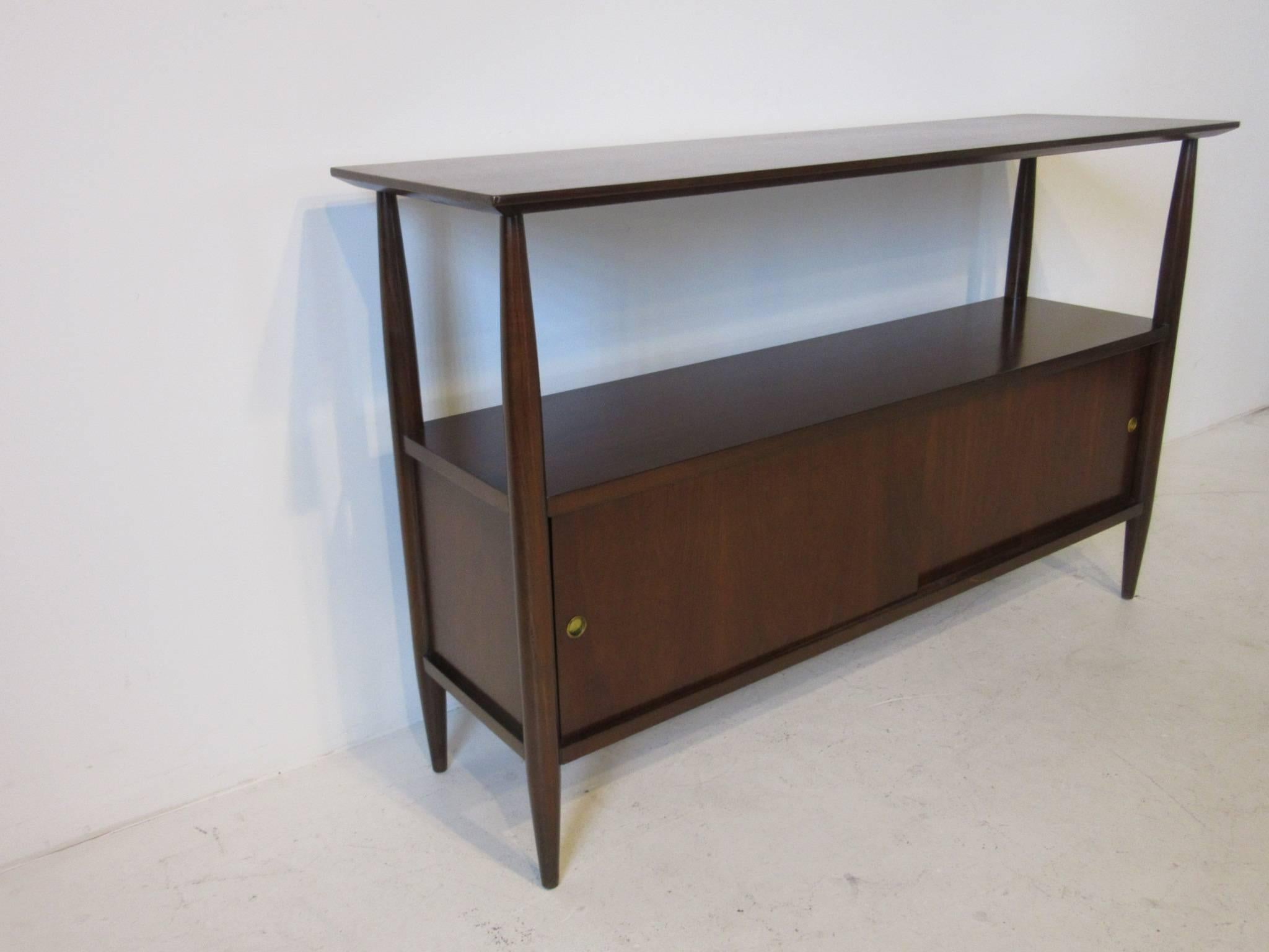 A dark walnut console or entertainment center with lower open storage, two sliding doors with storage area and finished back. This piece can be used in an entry way or in a media area for a flat screen or stereo unit and useful as a sever in a