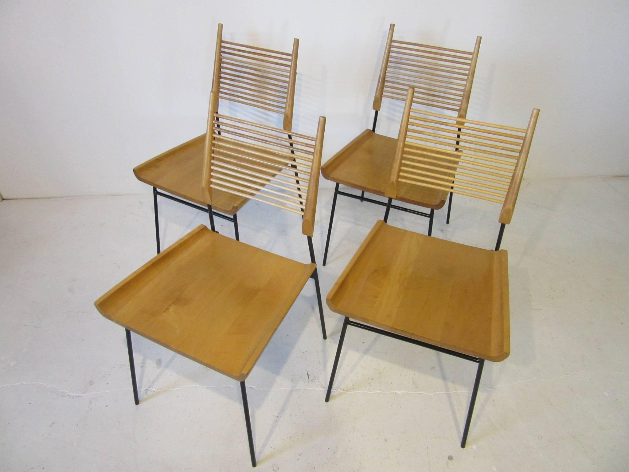 A set of four solid maple shovel seat or ladder back dining chairs with spindle design to the backrest , wood seat and satin black wrought iron frame with small rubber feet. Manufactured by the Winchendon Furniture Company from the Planner Group