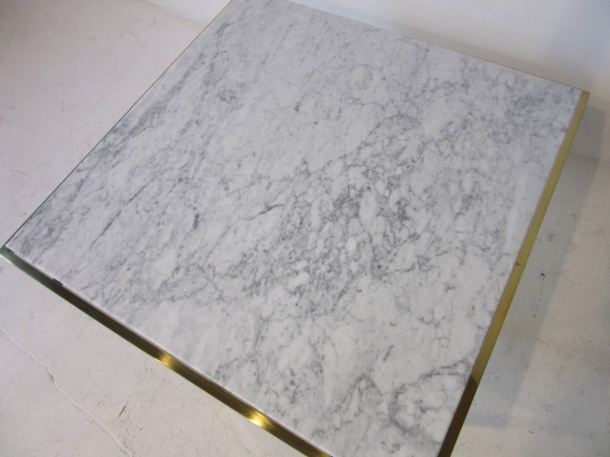 A square polished brass framed coffee table with a white and grey veined Italian Carrara marble-top in the manner of Milo Baughman.