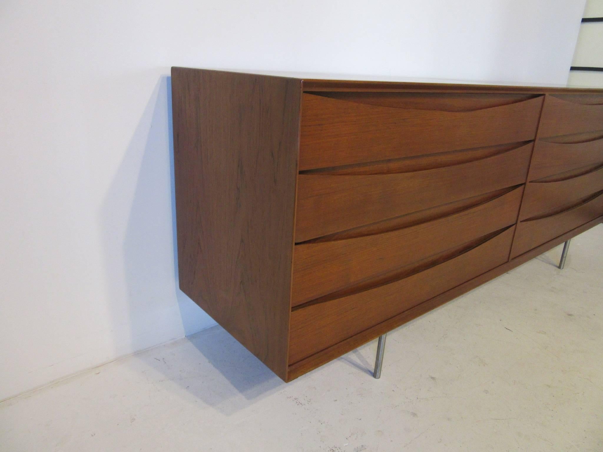 An eight-drawer dresser chest with distinctive cats eye Front Design que of Arne Vodder crafted in a medium toned teak wood sitting on stainless steel pole legs. Made in Denmark by cabinet maker Sibast.