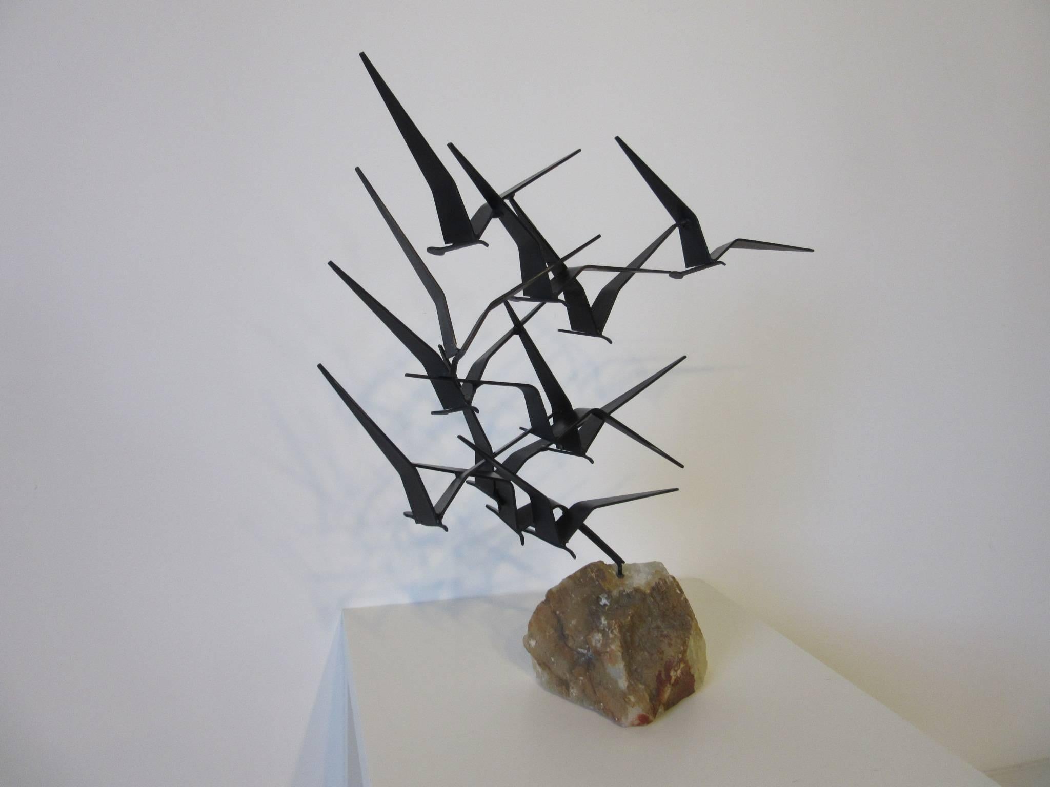 A welded metal flock of birds sculpture mounted on a natural quartz type stone with shades of brown tones, the birds are in a flat black finish and retain the artist signature and date to the wing of one. The sculpture is in two pieces the birds can