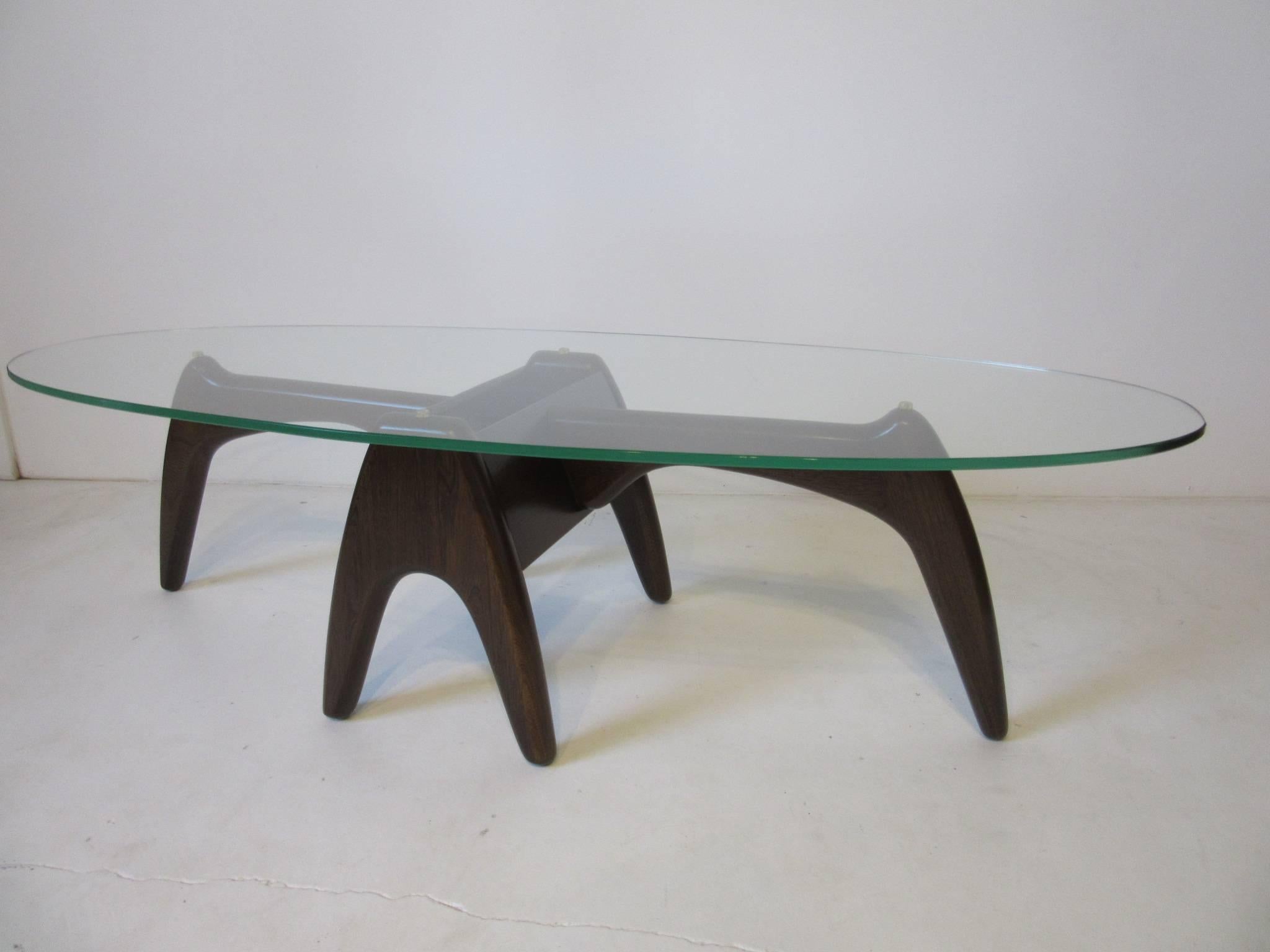 A dark walnut sculptural based coffee table with oval glass top.