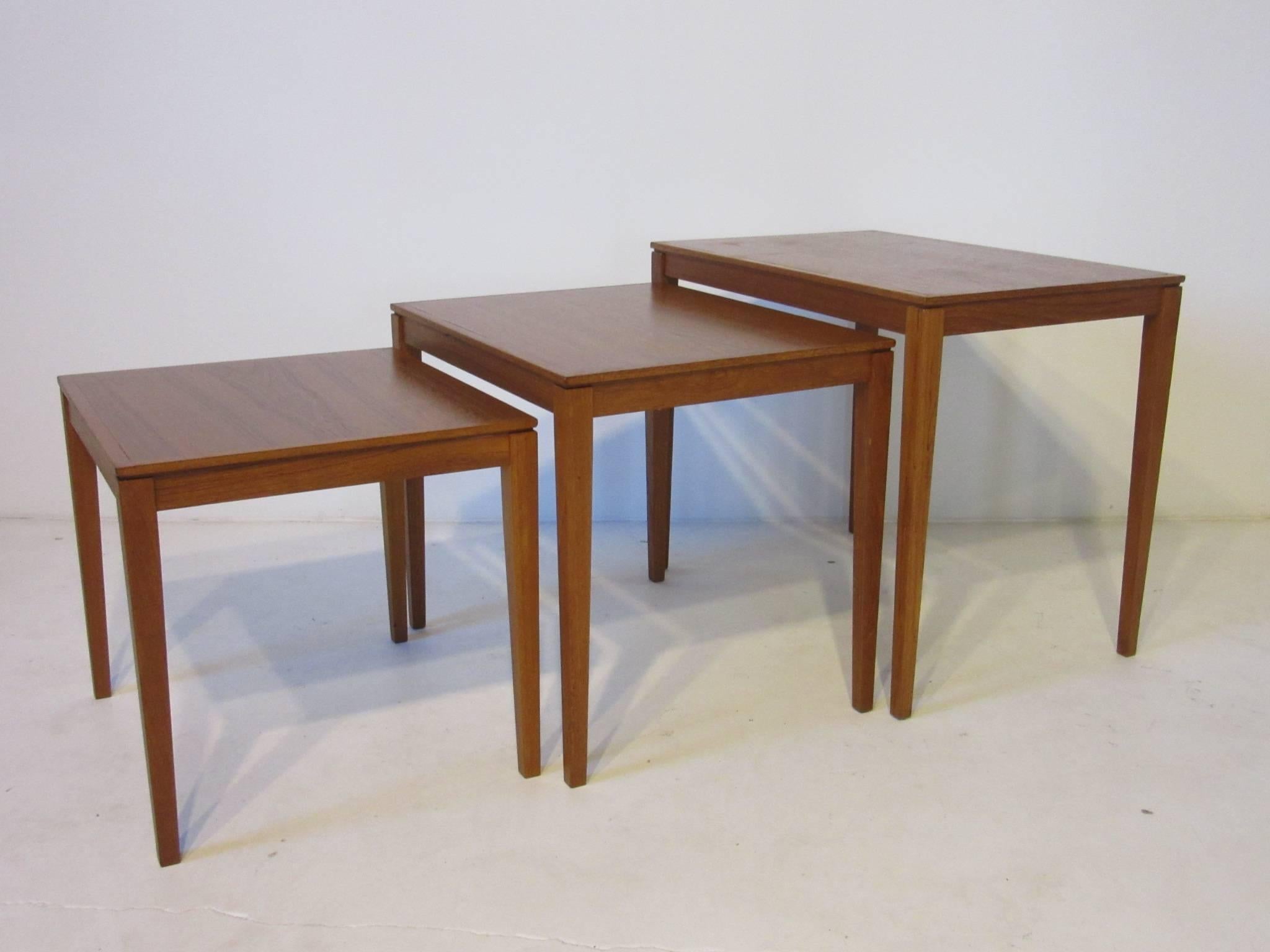A set of three teak wood nesting tables with well grained tops and tapering legs, made in Denmark and designed by Bent Silberg Mobler. The outer table size is listed below, the inner table measurements are 20.5