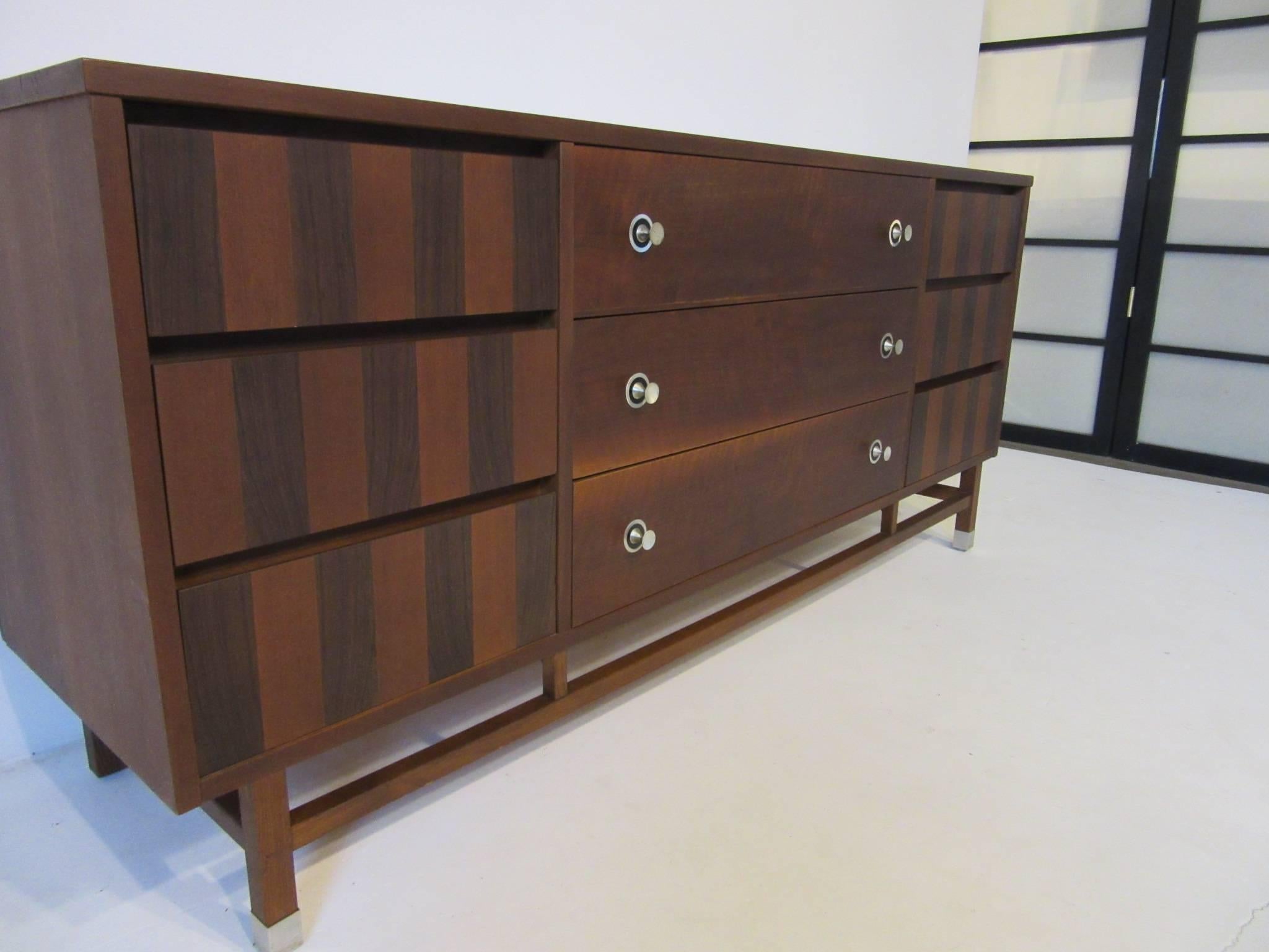 A midcentury nine-drawer dresser chest in dark walnut with rosewood details, spun aluminum pulls, lower stretches with matching aluminum leg caps.