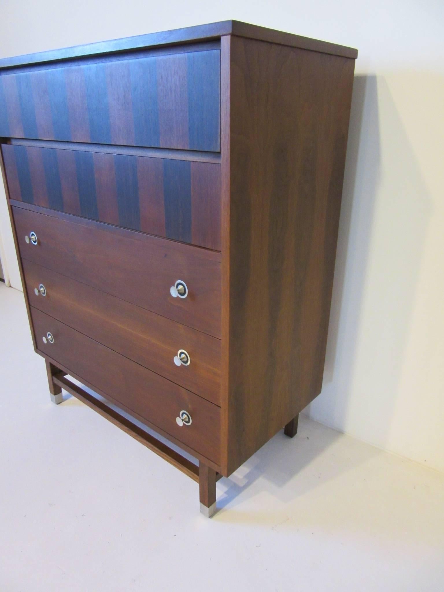 A dark walnut dresser chest with rosewood details, five drawers, aluminium turned pulls, one drawer with dividers and lower matching wood stretchers and aluminium capped legs. Manufactured by the Stanley Furniture company, their best and most