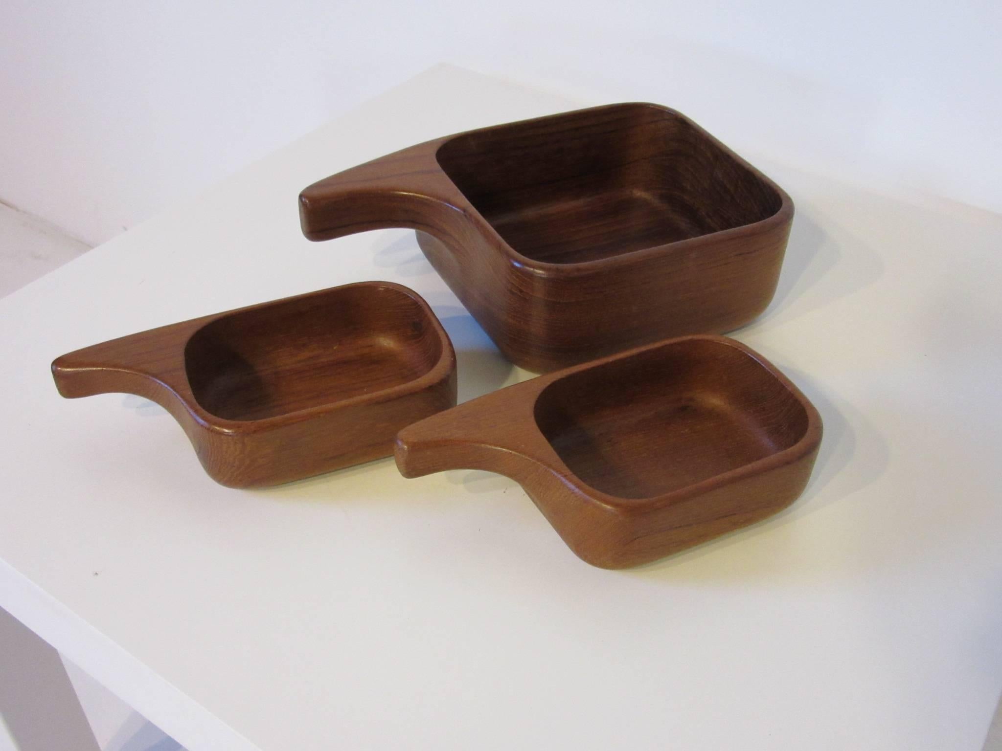 A set of three teak wood nut bowls, one large and two smaller with handles retaining the manufactures branded mark, AB Sowe Konst Sovestad, Sweden. The smaller bowl measurements are 7.13