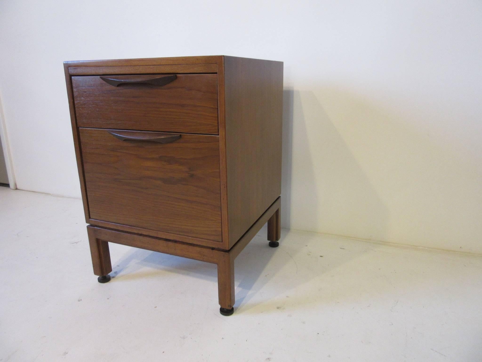 A stand alone medium dark walnut Jens Risom file cabinet with dark long walnut pulls and adjustable bronze toned foot pads. The cabinet has a smaller upper drawer and a lower full file drawer, could be used as a nightstand manufactured by Jens Risom