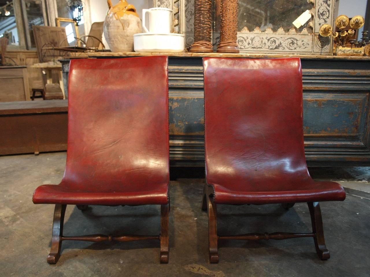 A terrific pair of early 20th century low sling back slipper chairs. Beautifully constructed in walnut and leather. Great nailhead detail. These chairs are very comfortable.