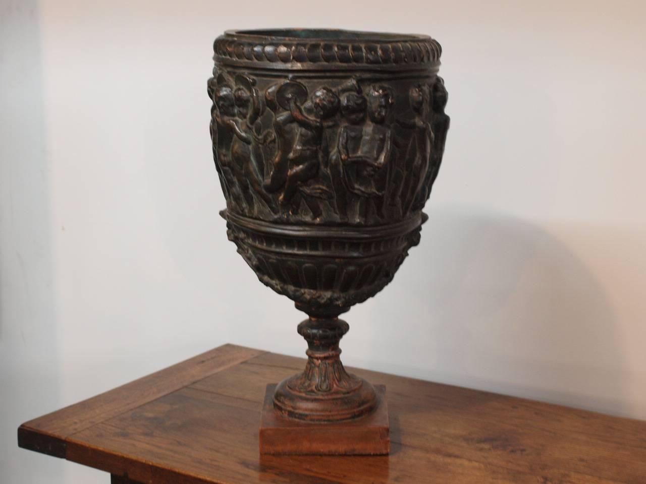 A stunning 19th century patinated terracotta urn from Northern Italy. This magnificent urn is adorned with festive putti, or cherubs, playing musical instruments in celebration, all raised on a square base. This is a spectacular piece, especially