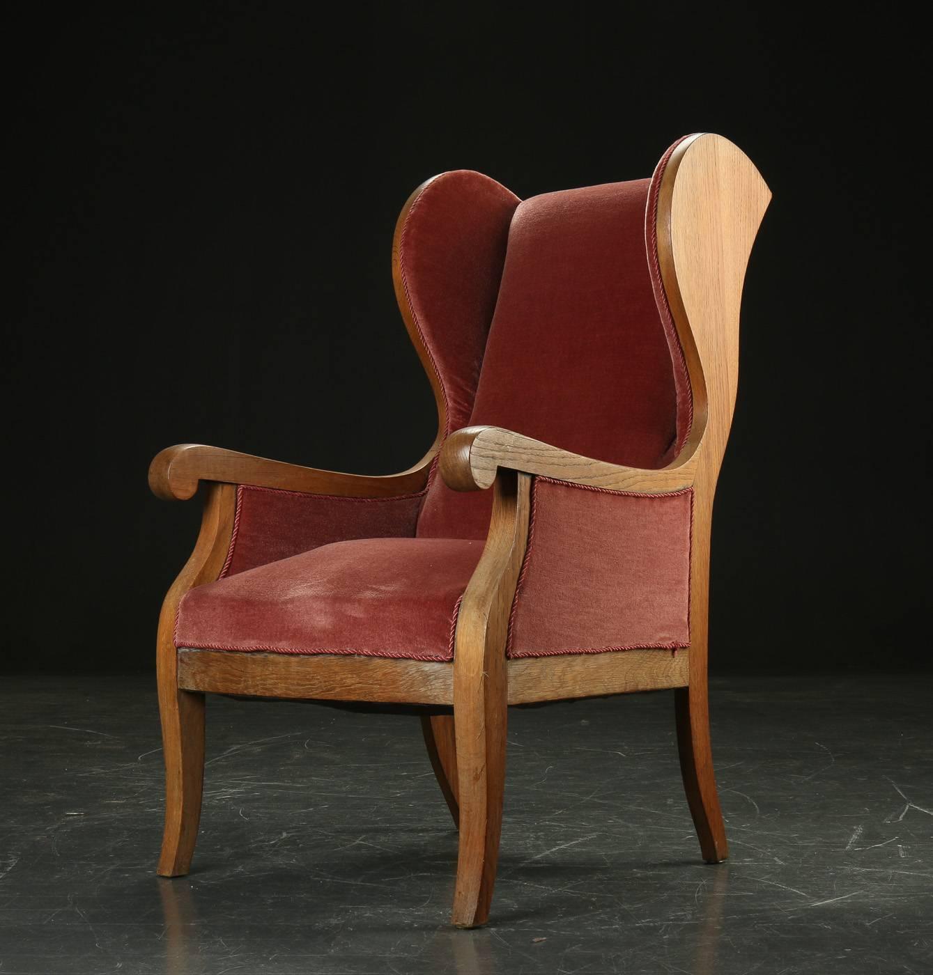 Sexy 1940s wingback armchair by Frits Henningsen with sweeping arms and curved headrests. Frame of oak. Velvet upholstery is elegant but shows its age.