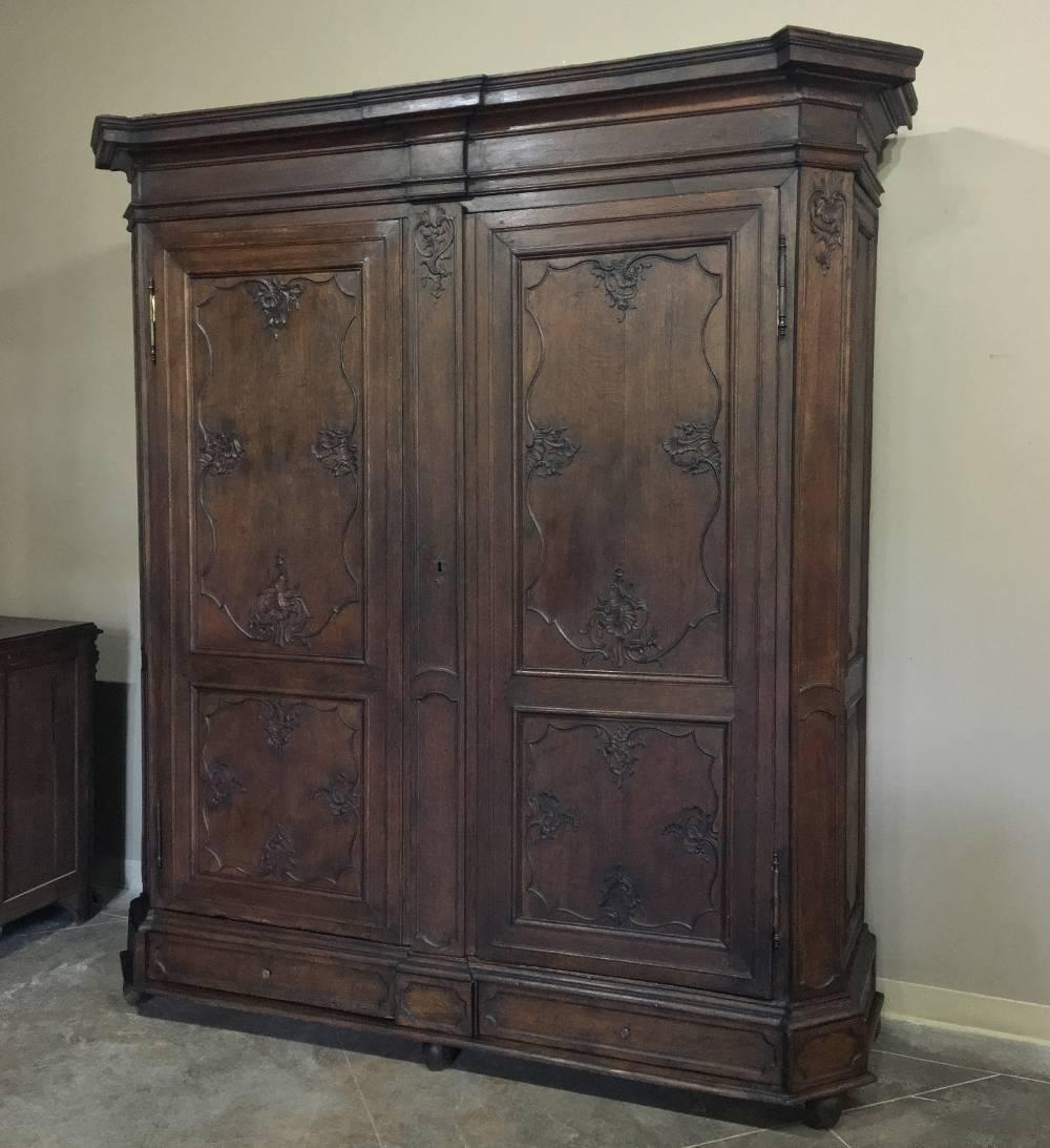 Grand 18th century hand-crafted from dense, old-growth French white oak in the Lorrain Chateaux region, this handsome Country French armoire features mitered cornerposts, bold molding, and Baroque-inspired hand-carved detailing. Lower drawers add