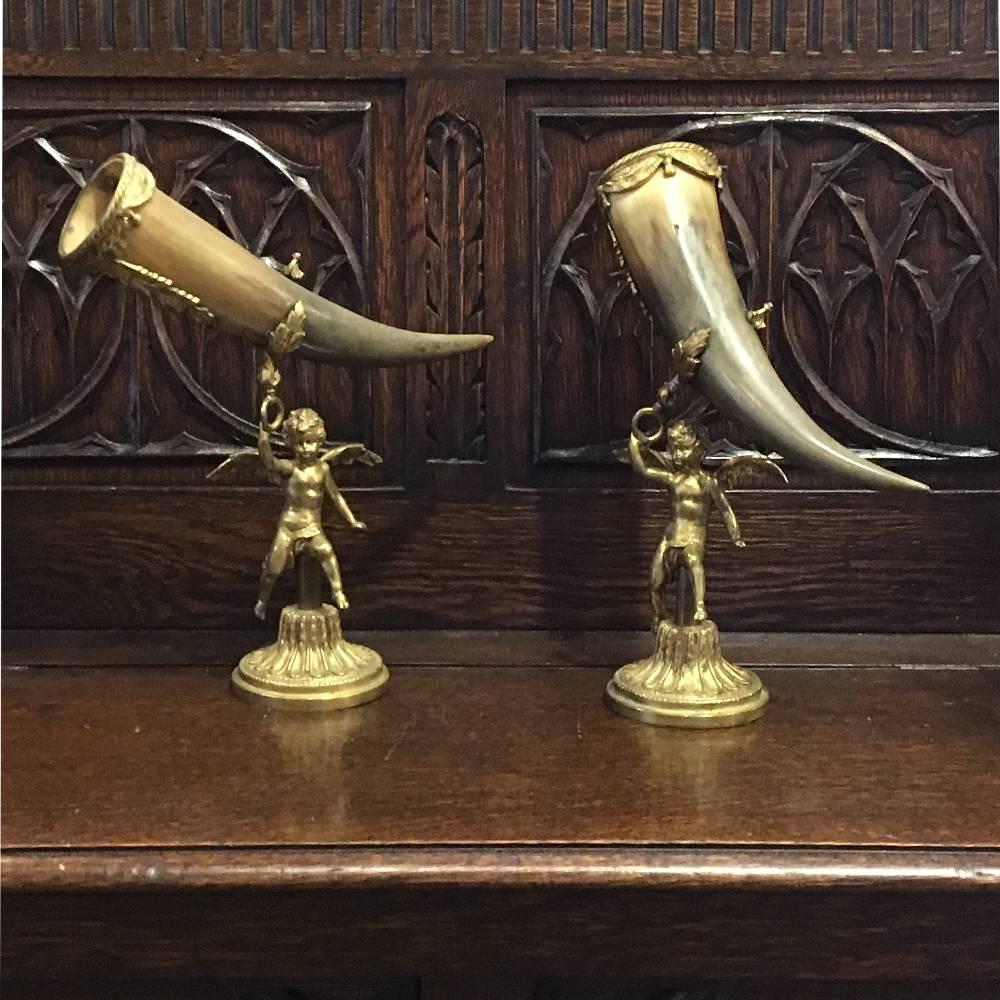 Pair of 19th century bronze-mounted trophy horns features winged cherubs in a classic running pose, set upon cast bronze bases depicting classically styled inverted lotus blossoms. Cow horns feature intricately cast rings with acanthus floret