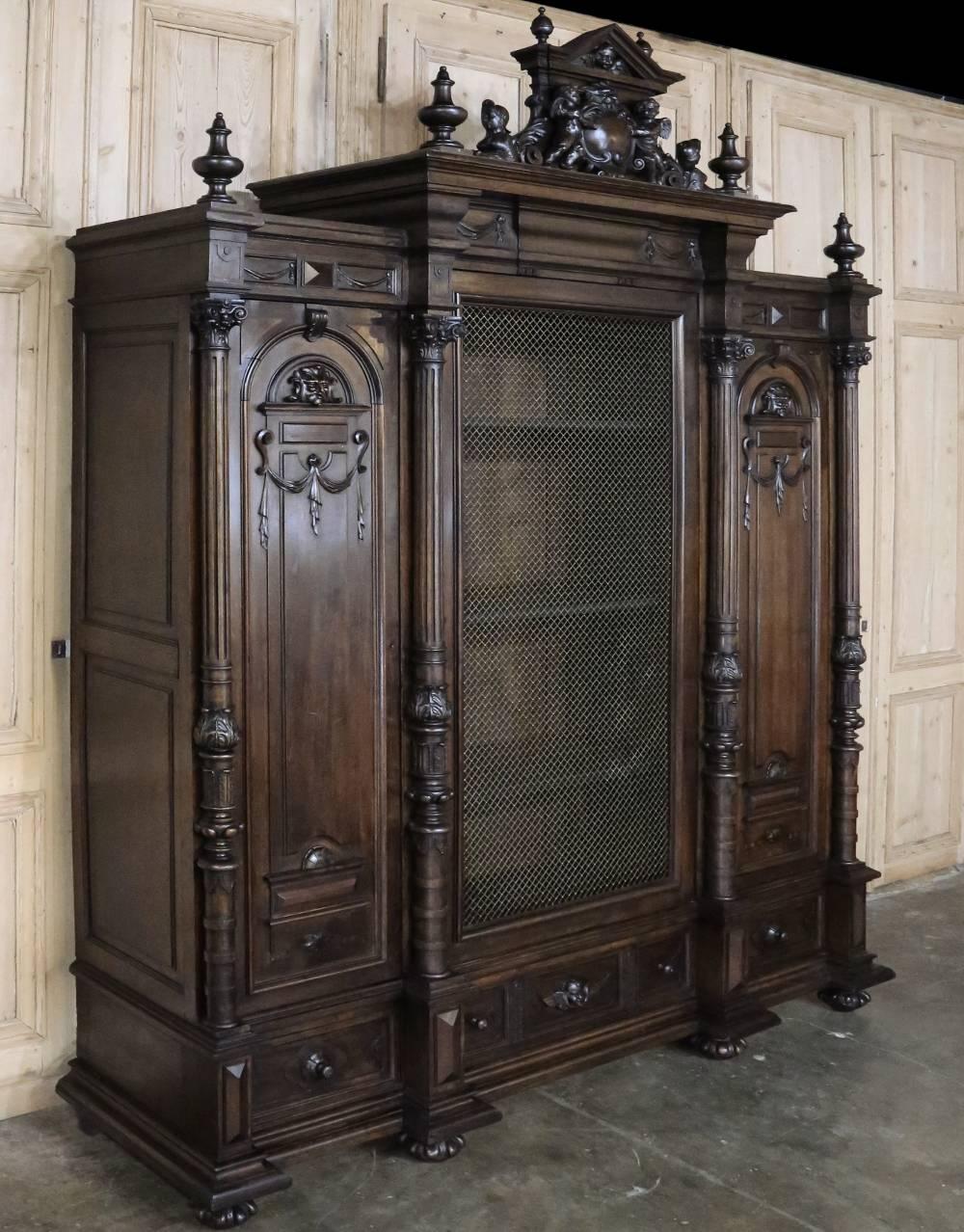 Resplendent with sculpted angels and classical architecture, this stupendous 19th century Italian Renaissance triple armoire was fashioned from solid walnut and features an impressive crown punctuated by two sizes of turned finials, elaborate and