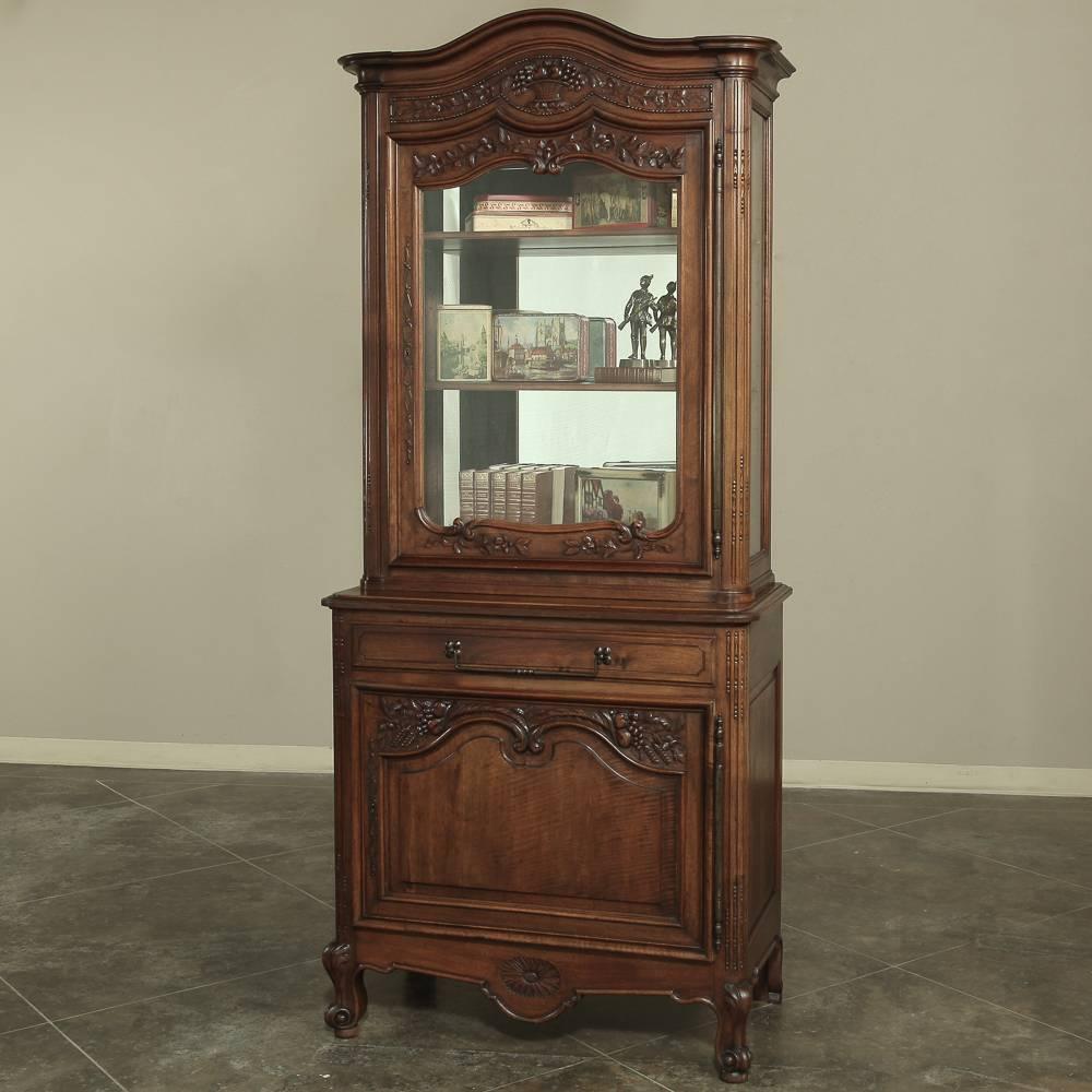 19th century country French neoclassical walnut vitrine features classical embellishment hand-carved into the sumptuous French walnut with the added grace of curvaceous French scrolled designs in the crown and door panels and legs. Original