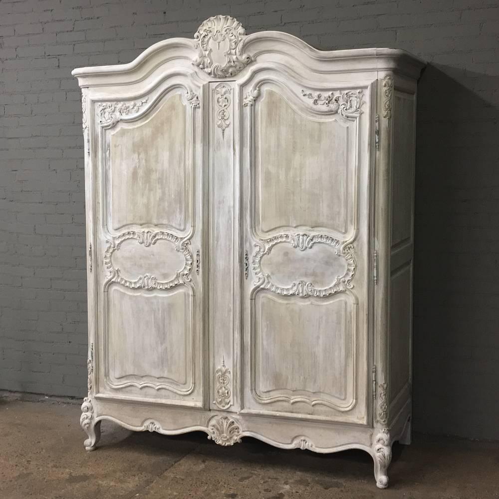This stunning 19th century Country French Regence whitewashed armoire features exquisite hand-carved detail in glorious relief from the arbalette crown to the scrolled apron below, all rendered by a master sculptor! The crown, which resembles an
