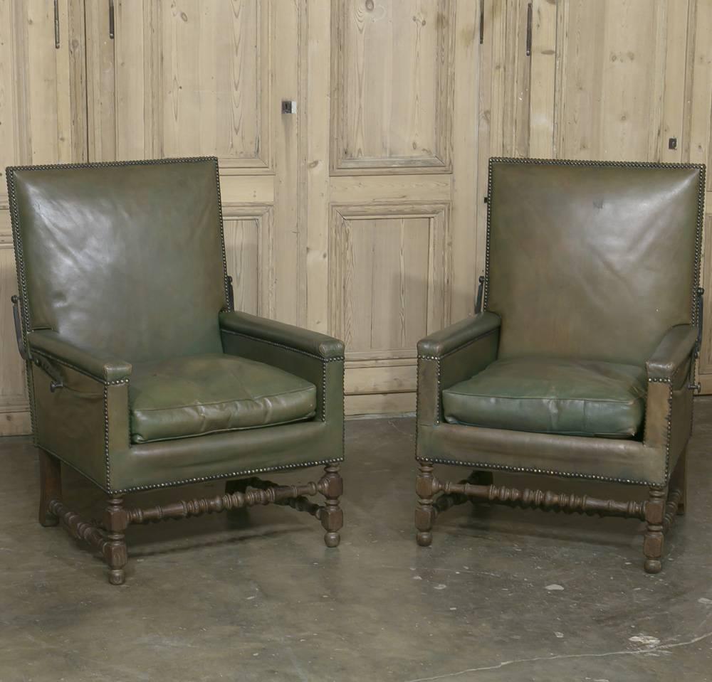 Lounge with style in this pair of Mid-Century Modern leather reclining armchairs. Each armchair sits on sturdy turned oak legs and is upholstered in elegant green leather finished with a nailhead trim. Convenient side pouches are perfect for holding