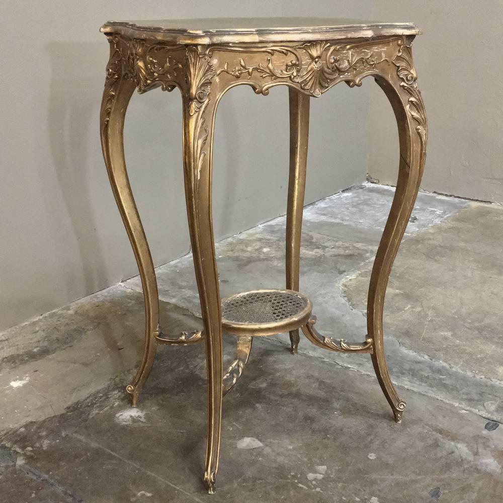 This gorgeous 19th century French Louis XV giltwood table features elaborate hand-carved detail in the contoured aprons and boldly scrolled cabriole legs, featuring a raised caned oval shelf below and a contoured and beveled top above, all finished