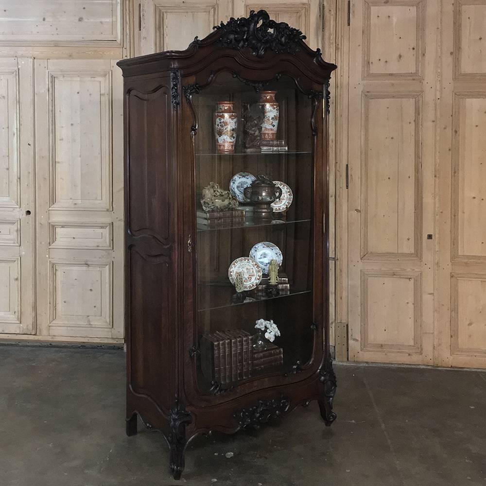 This exceptional 19th century French Louis XV Rococo walnut display armoire ~ bookcase displays a remarkable work of the wood sculptor's art, rendered in the naturalistic form of the rococo genre reflecting an appreciation for the bounty of God and