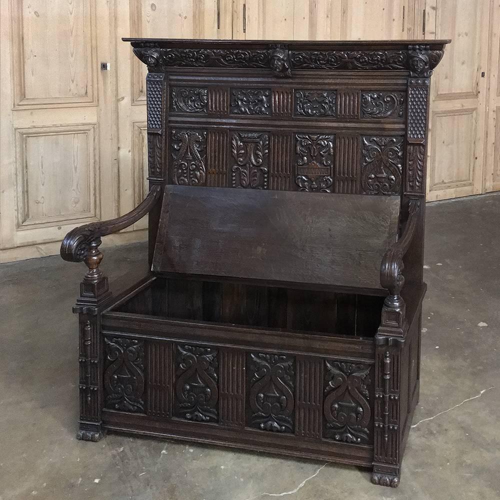 This stunning 19th century French Renaissance hall bench features no less than 15 different panel designed hand-carved into the seatback and front of the trunk below! Gracefully scrolled armrests with acanthus leaf and rosette carvings provide