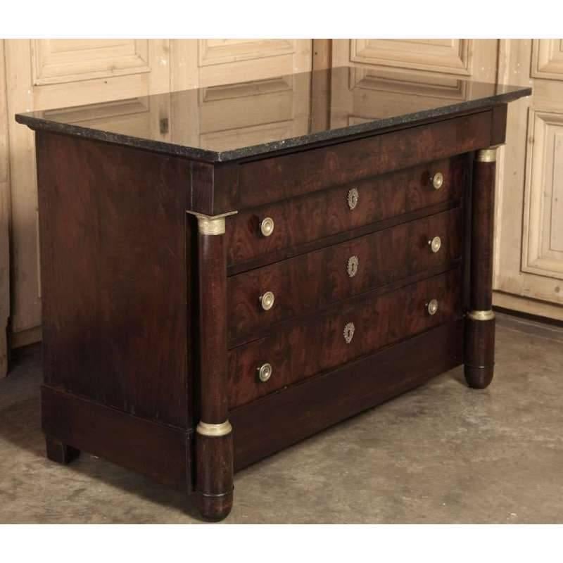 This handsome Antique French Empire Period marble-top commode with the tailored lines of the Classic style featuring a black marble top, flame mahogany façade and cast bronze gilded accents, pulls and key-guards, this commode dates to the Empire