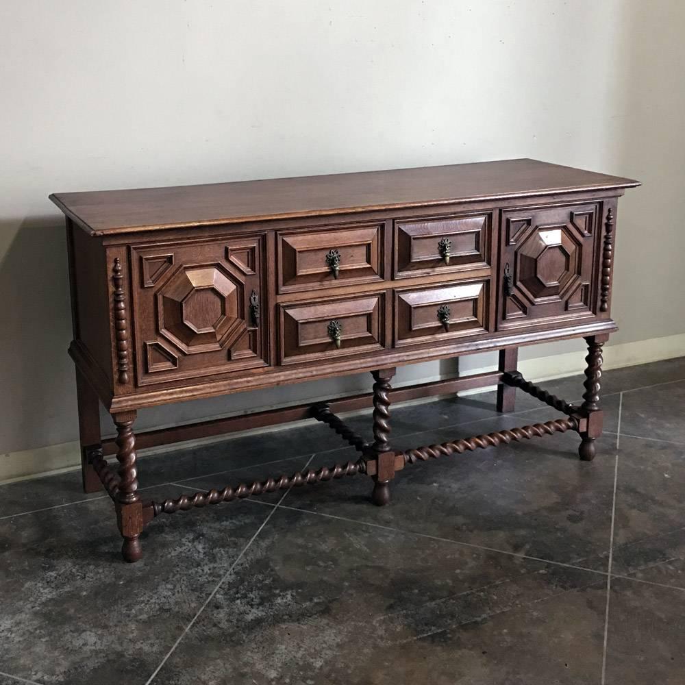 This excellent example of the style, rendered in solid oak, is a well preserved Antique Jacobean Buffet, set upon urn pediments, adorned with geometric molding and fitted with its original cast bronze key guards and drawer pulls. Barley twist legs