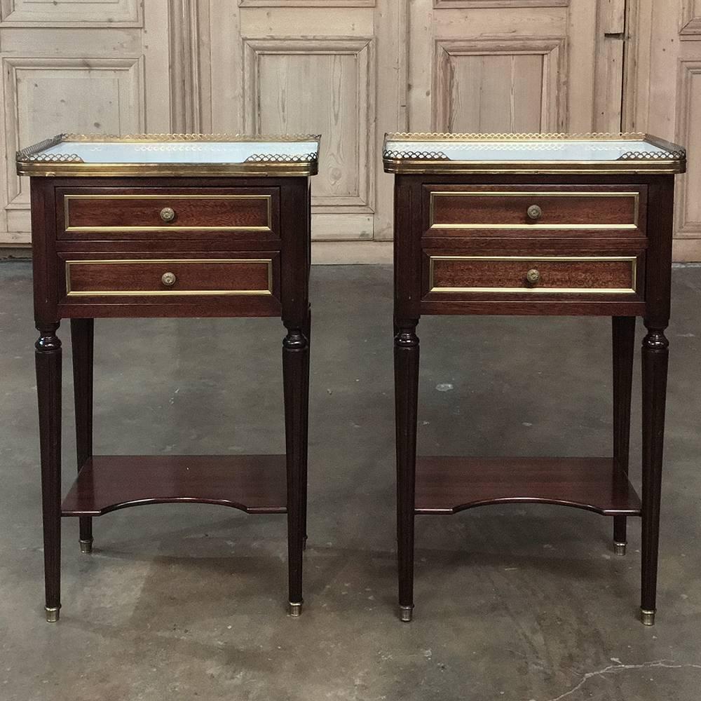 This pair of French Maison Jansen Louis XVI style marble-top nightstands are a uniquely French expression of the style, handcrafted from fine mahogany with pierced brass railing around the Cararra marble tops. Tapered legs with a lower shelf below