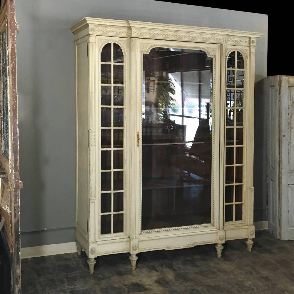 19th century, French, Louis XVI painted triple bookcase, display armoire features a stately elegance with original painted finish surrounding beveled unfettered glazing on the center door flanked by multi-paned side panels with no less than 18 panes