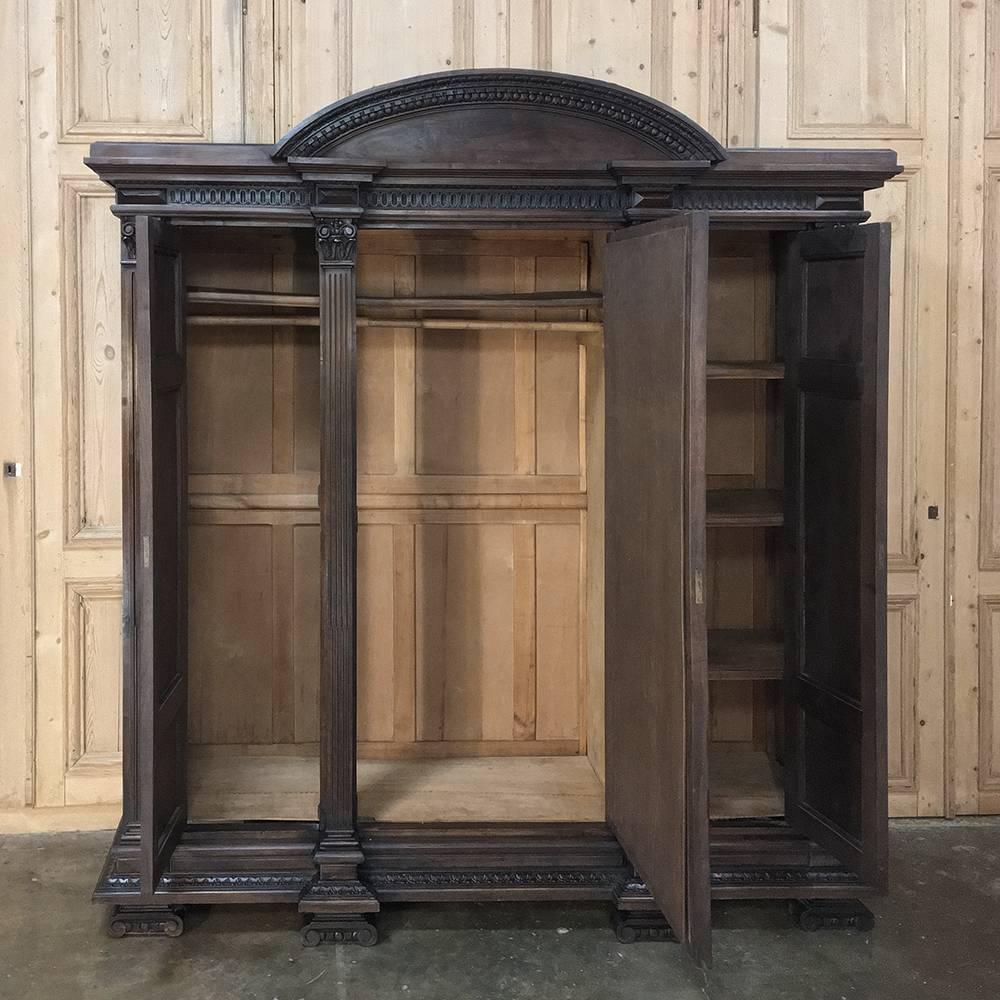 Antique Italian walnut neoclassical triple armoire is unusually short for such a design, probably specified by the owner who ordered it to accommodate a lower ceiling in a particular room. Full length center door mirror is flanked by side doors