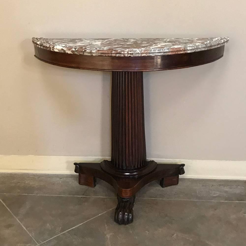 Although it features a tripod base and fluted column, all rendered from exotic imported mahogany, this elegant and rare 19th century Louis Philippe period demilune marble-top console was designed to sit against the wall, with a half-moon shaped