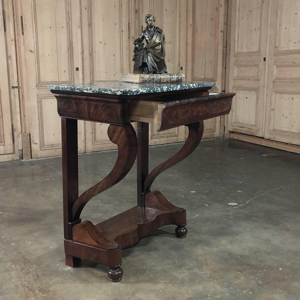 Representing the essence of the style, this 19th century, French, Louis Philippe mahogany marble-top console features tailored lines including scrolled front legs and a full-width concealed drawer. A contoured display shelf appears below, and the