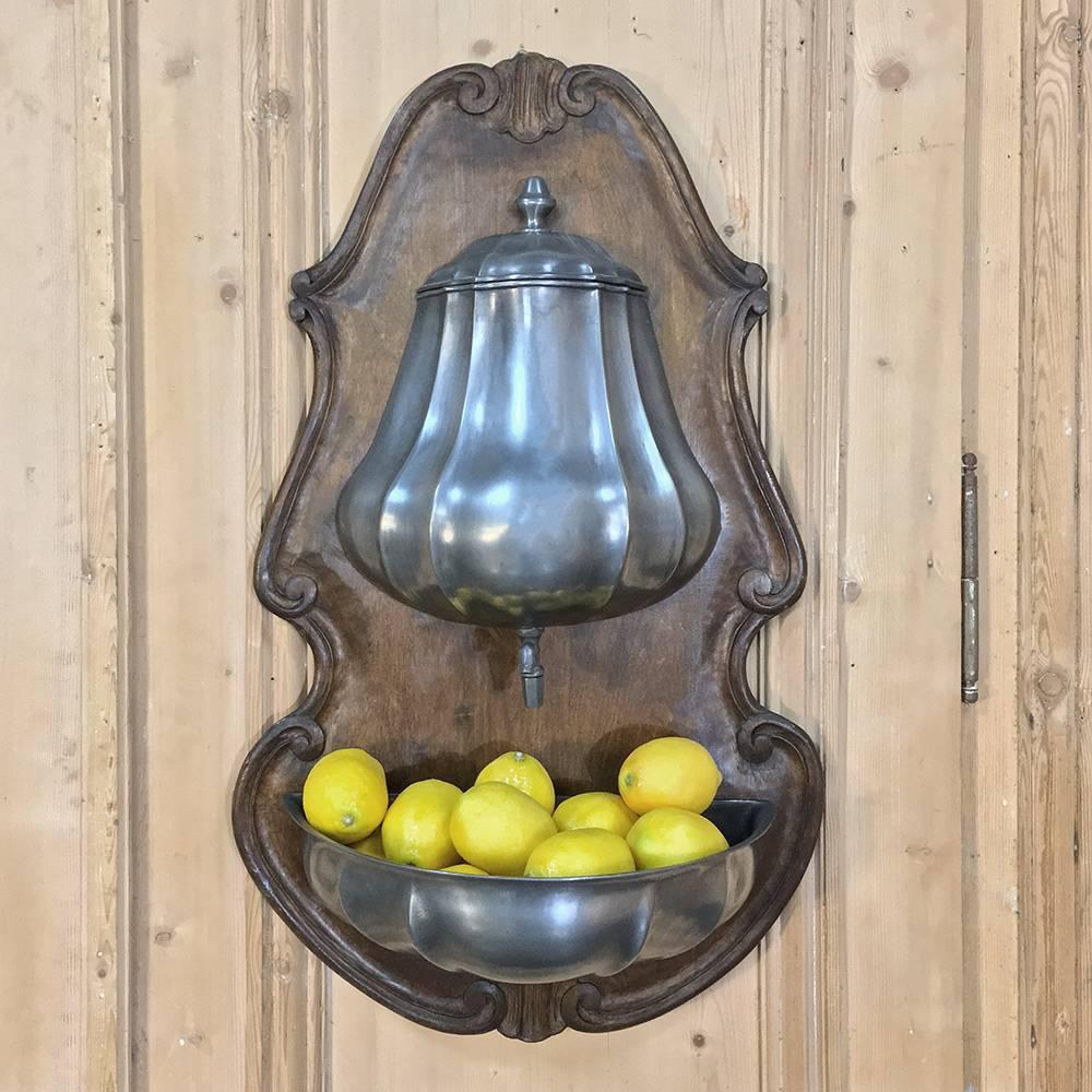 This charming 19th century Pewter wall fountain features its original hand-carved wall plaque and Pewter reservoir and basin, and was originally designed to hang just outside the back door so the family and workers could wash up before entering the