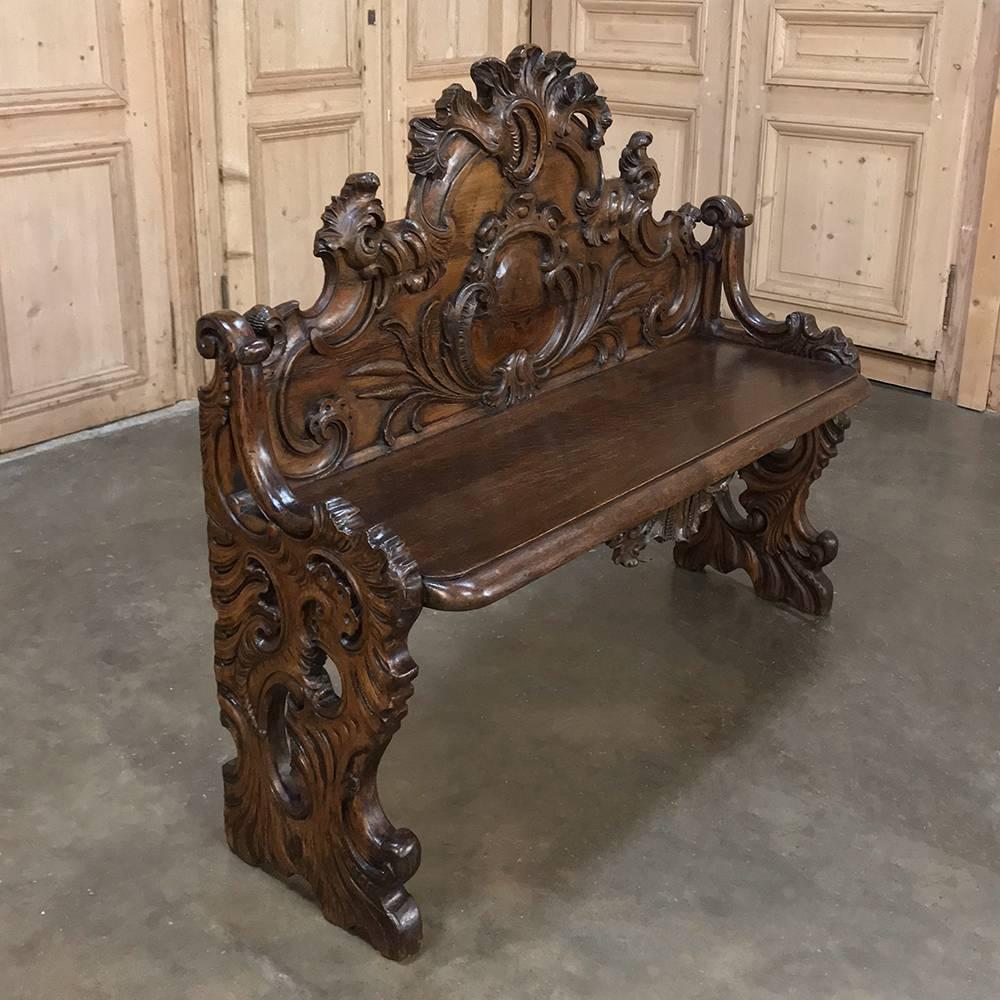 19th century Italian Baroque walnut hall bench is a splendid example of the genre, with magnificent heraldic crest taking center stage on the exquisitely sculpted seatback, with equally impressive side supports, all pierce-carved to perfection with